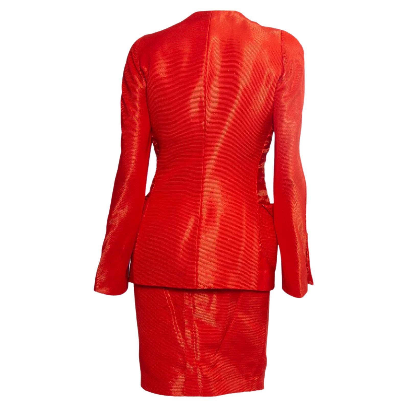 Presenting a bright orange runway skirt suit masterpiece, designed by Gianni Versace. This skirt suit was debuted as look 11 on the Gianni Versace S/S 1991 runway. Metallic threading creates a shiny effect throughout. The blazer creates an hourglass