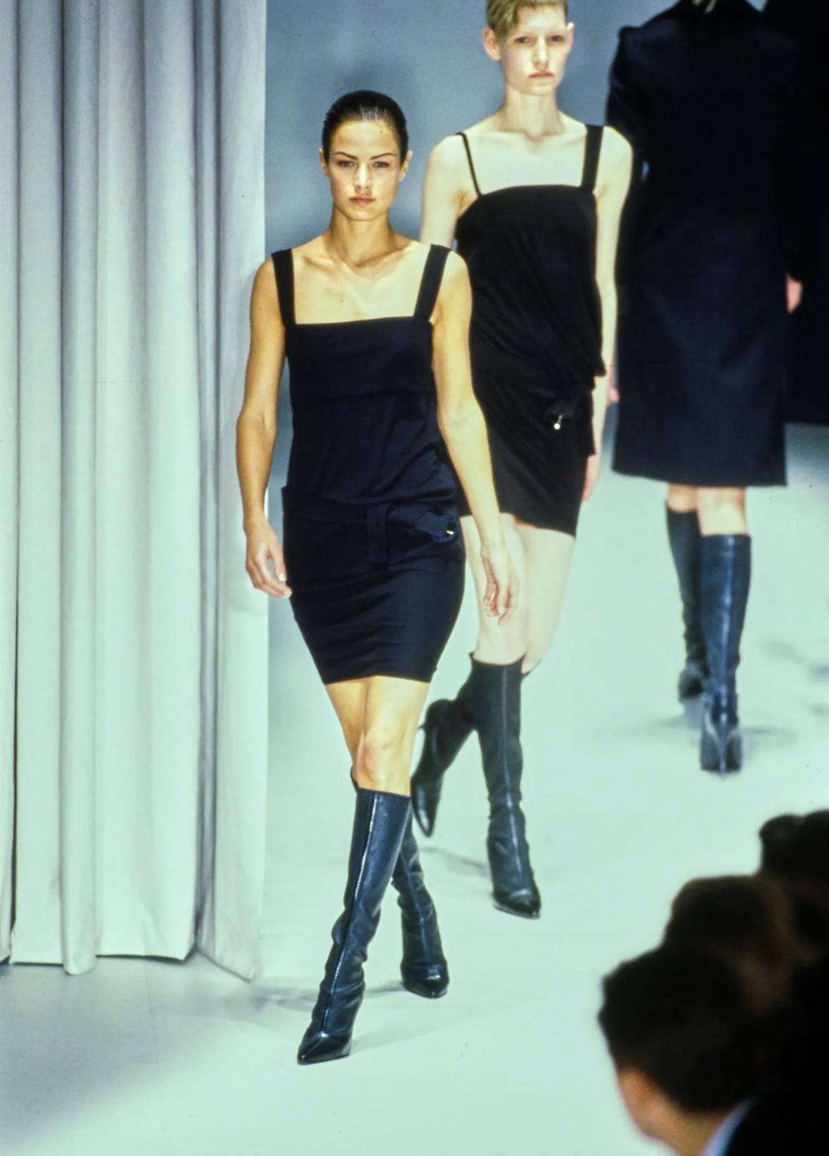 Wir präsentieren ein sinnliches schwarzes Gianni Versace-Cocktailkleid, entworfen von Gianni Versace. Dieses kleine Schwarze aus der Herbst/Winter-Kollektion 1997 hat breite Träger und einen quadratischen Ausschnitt. Das Kleid ist mit einem