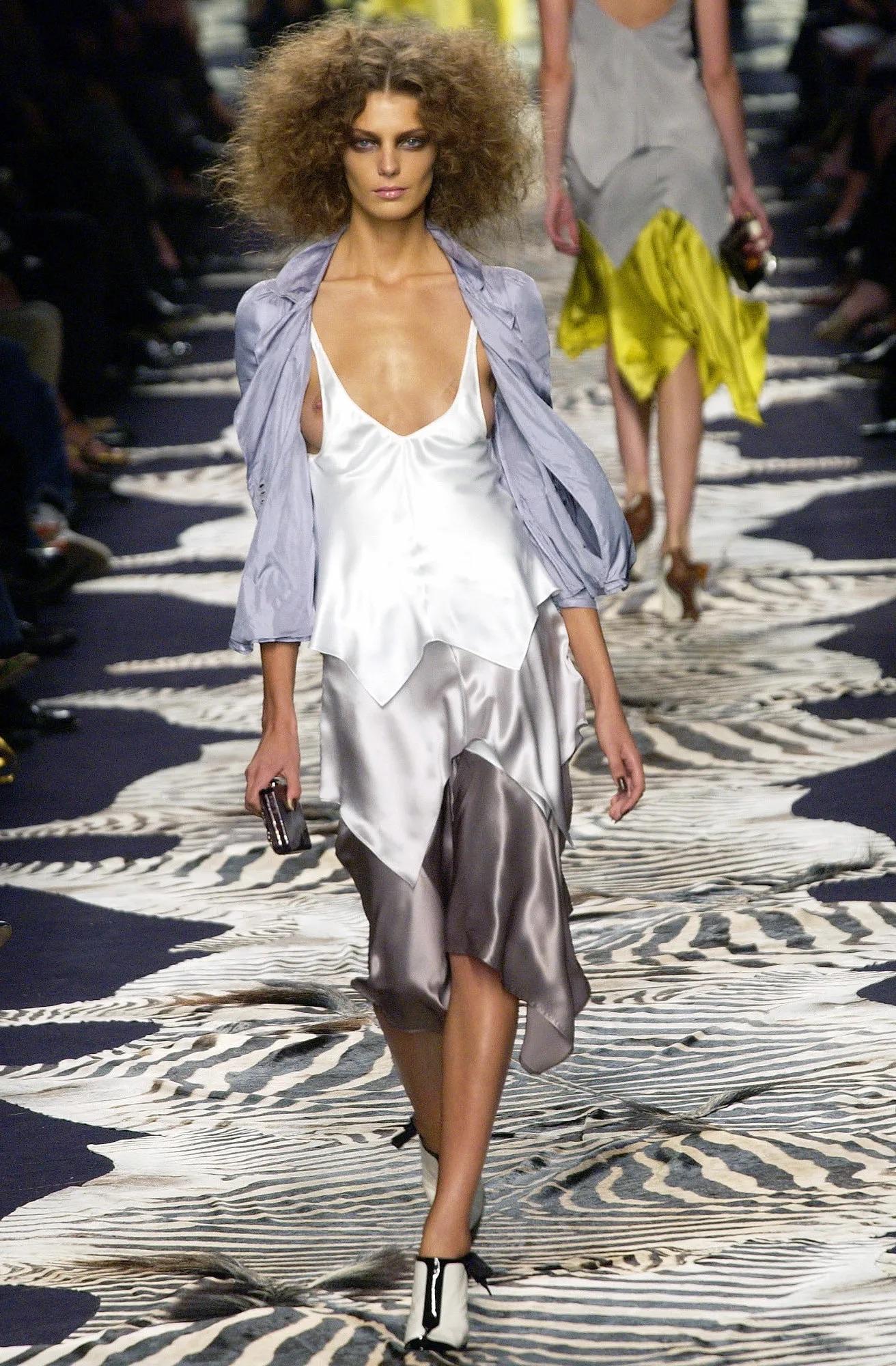 Questo abito in raso di Yves Saint Laurent Rive Gauche, disegnato da Tom Ford, appartiene alla collezione Primavera/Estate 2004 e ha debuttato come look 22 su Daria Werbowy. Presenta un design a fazzoletto con scollatura a palloncino e spalline.