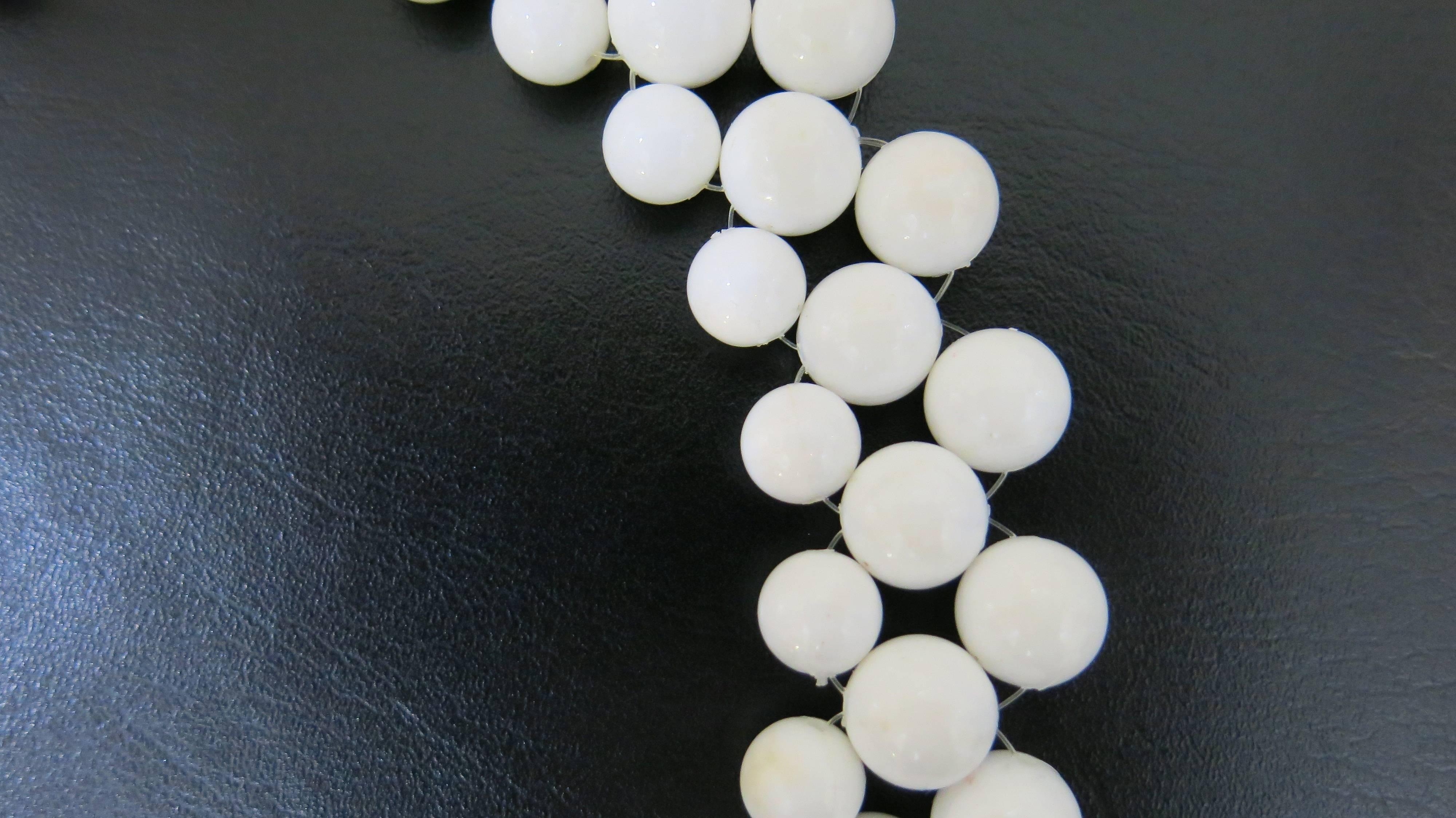 White plastic bead necklace with gold tone flower at center. Flower is stamped with the designer name as well as "1972". There is some slight discoloration on a few of the beads but it is barely noticeable. Necklace lays close to the