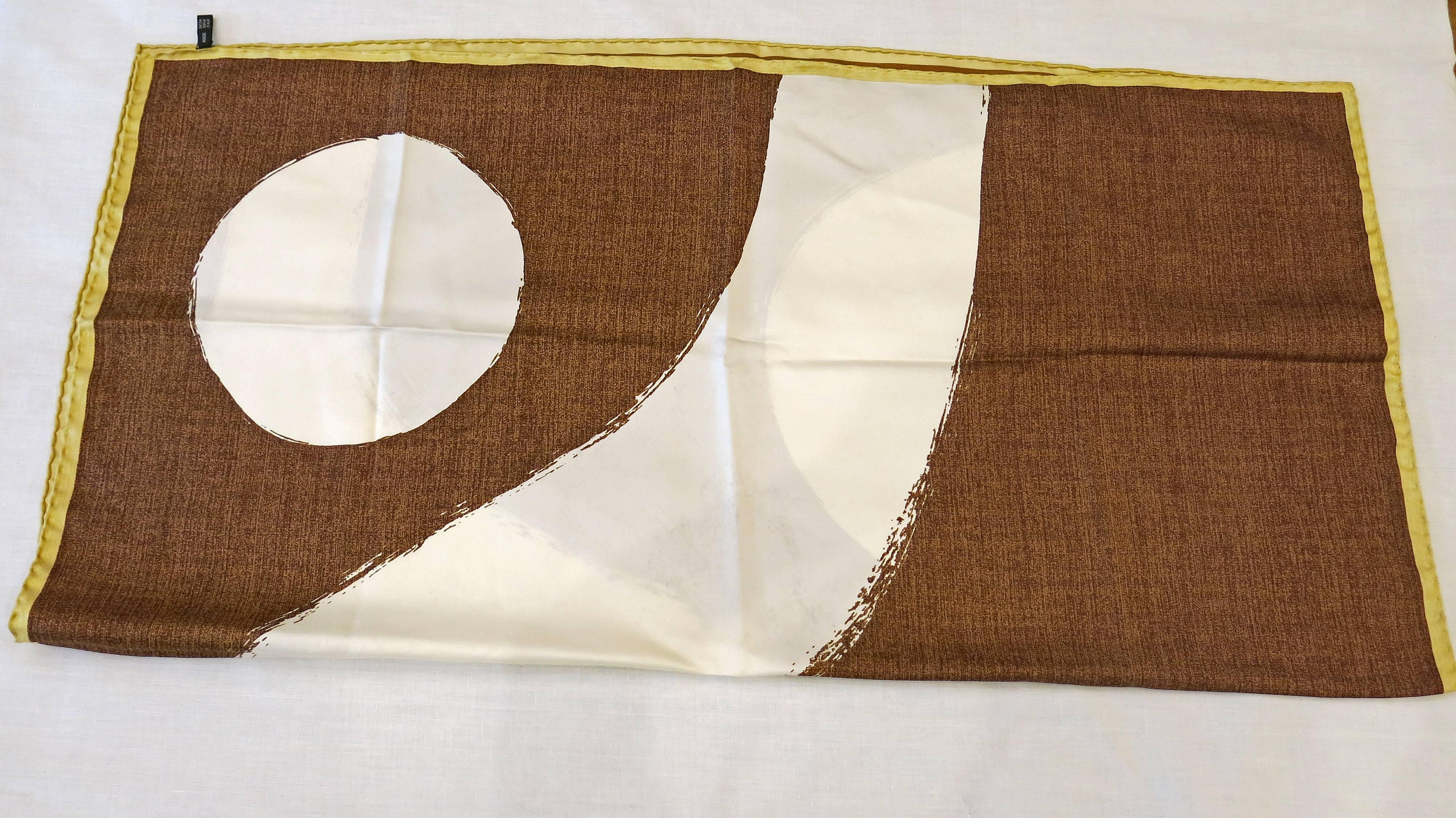 Cream brown and gold colored silk scarf with a design that imitates texture as well as two cream colored circles and a diagonal line that splits the two sides of the scarf in half. This design is reminiscent of a yin yang symbol. Scarf is gold
