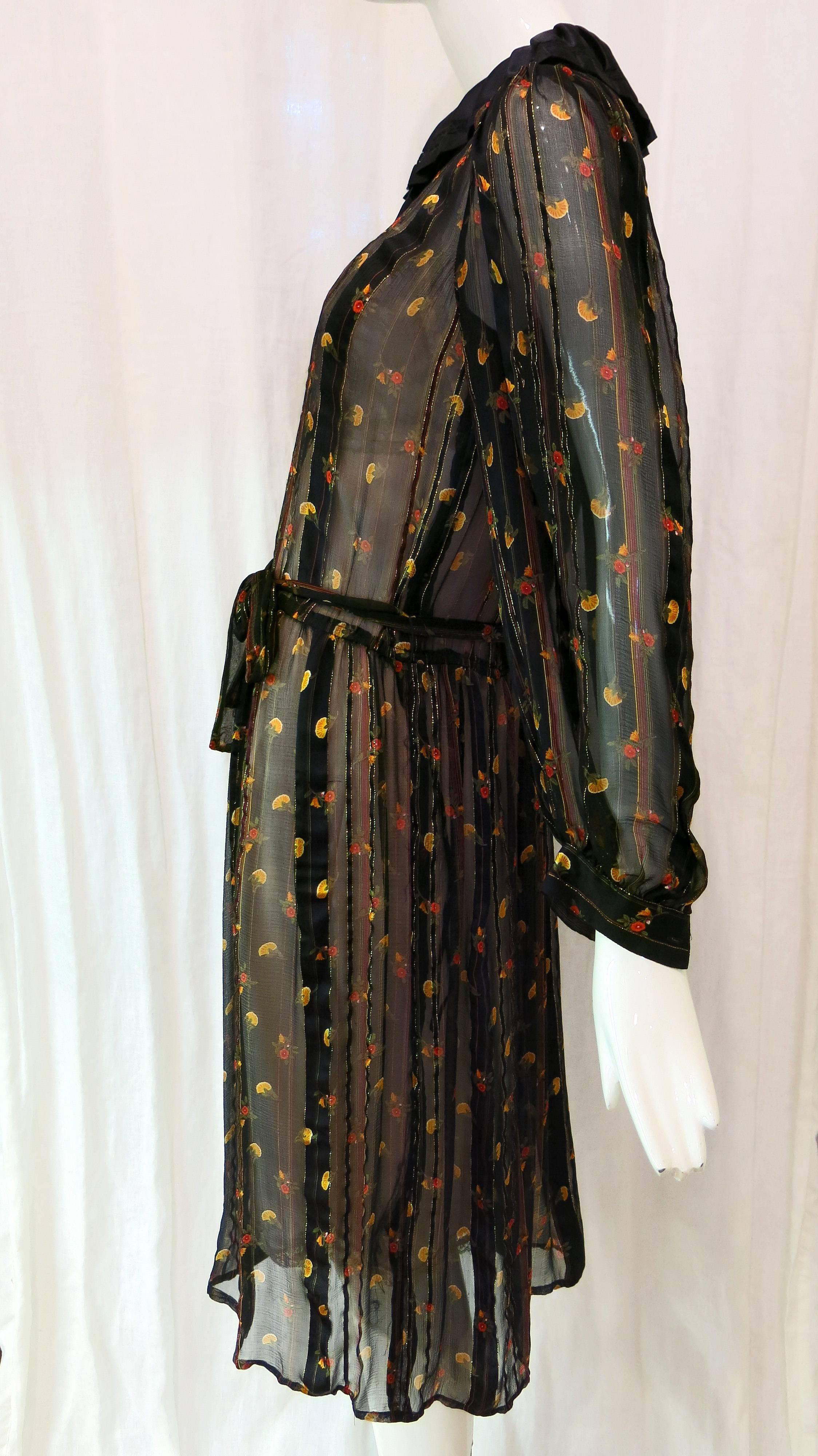 Black sheer floral button down dress. Belts at waist where buttons end. Elaborate pleated collar with ribbon bow. Five covered buttons to waist. Metallic gold stripes throughout. Buttons at cuffs. Dress hits at the knee. 

Jack Mulqueen was known as