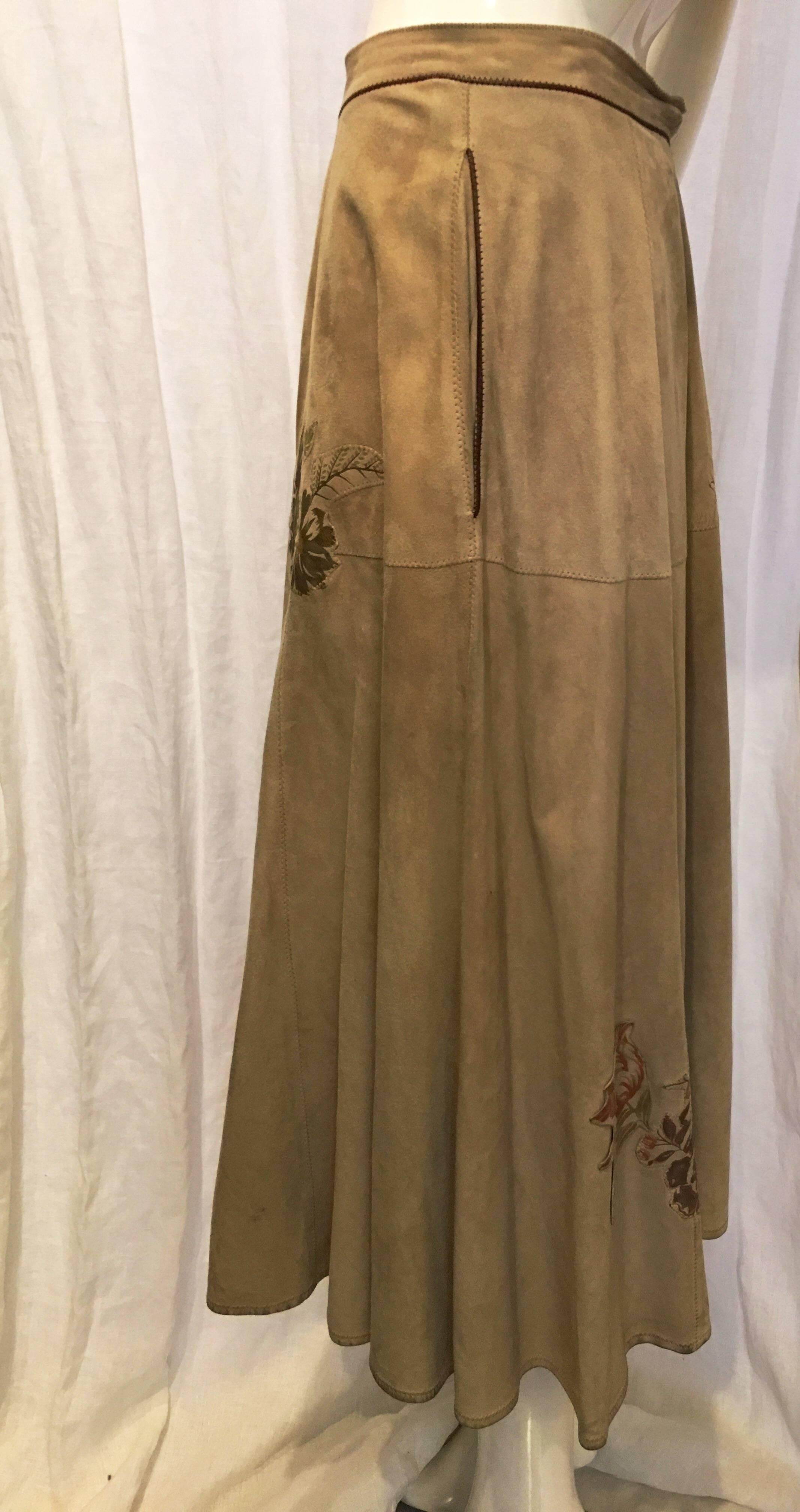 Tan suede skirt with floral patches. Two front pockets. Front zip and snap floral button. A line style fit. Back of garment goes out slightly at the waist. Some slight discoloration and wear to the suede as a result of age. Please note pictures for