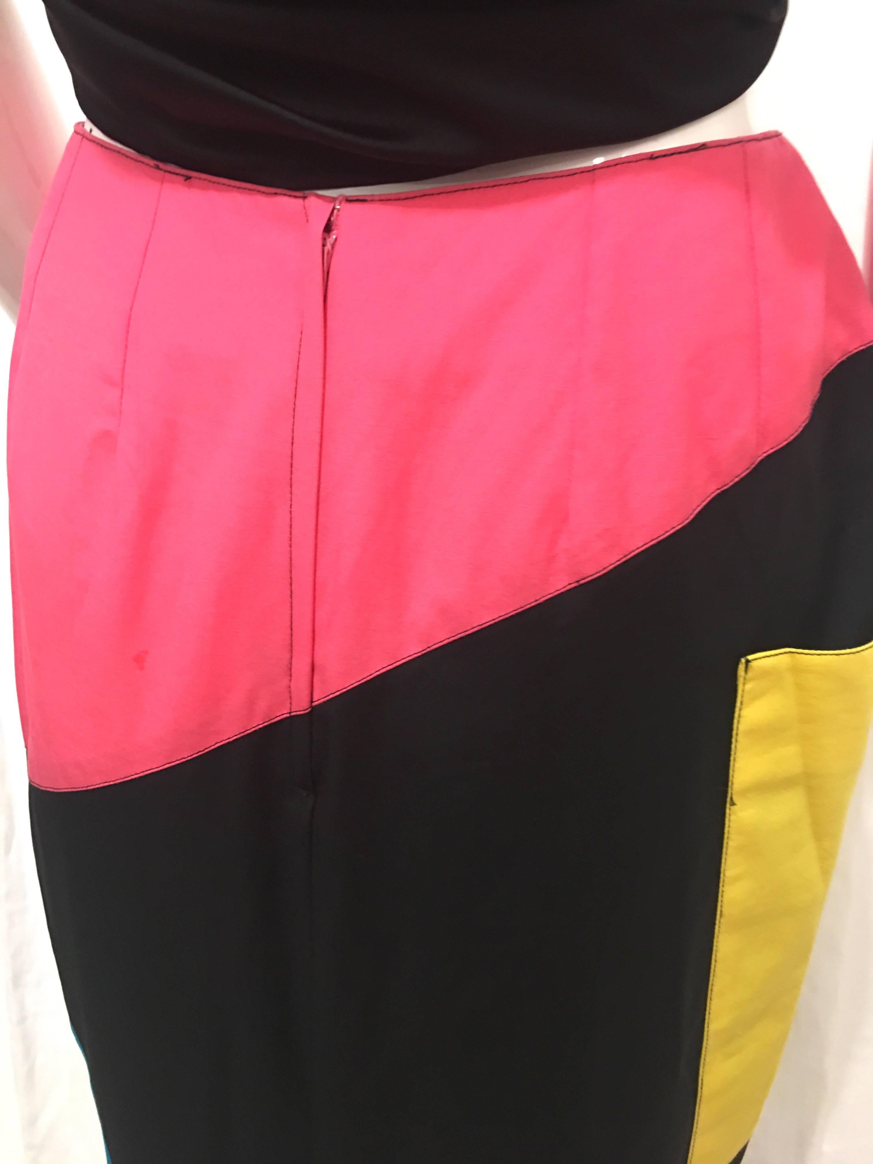 High waisted black pencil skirt with blue yellow and pink colorblock segments. Yellow segment is an oversized pocket that wraps around the side of the skirt. Hits right above the calves. Slit up the back to the bottom of the thighs allows for easier