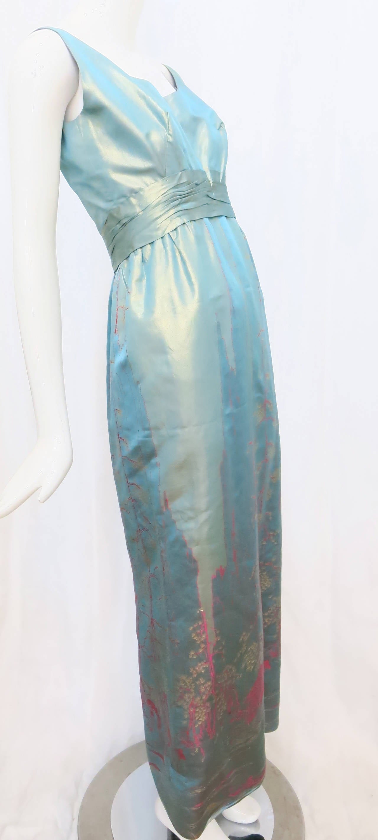 This vibrant, shimmering embroidered 1950s silk taffeta column dress features a Japanese inspired motif with a gathered empire waist. The front of the dress showcases a scalloped collar and plunges down the back. Darting at the bust and a slit in
