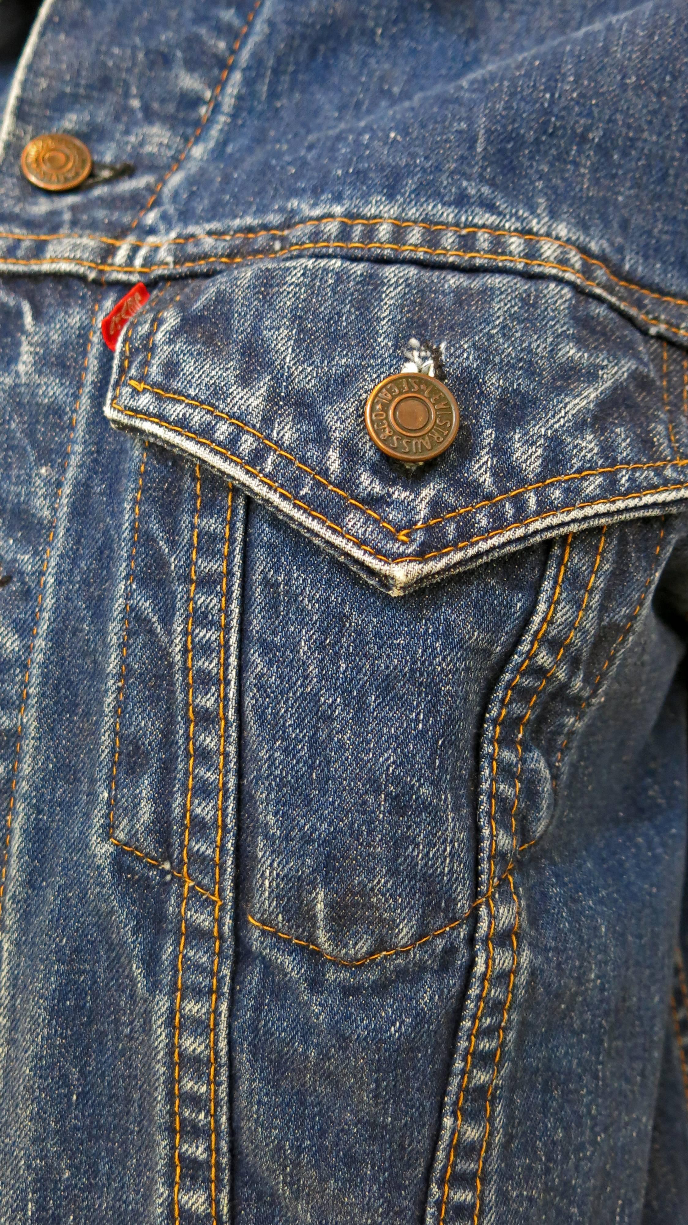 Indigo wash Levi's classic denim jacket. In the center of the back of the jacket there are two palm trees, the sun water and grass are embroidered. Has two breast pockets. Some fading throughout as a result of age. Some holes forming at the