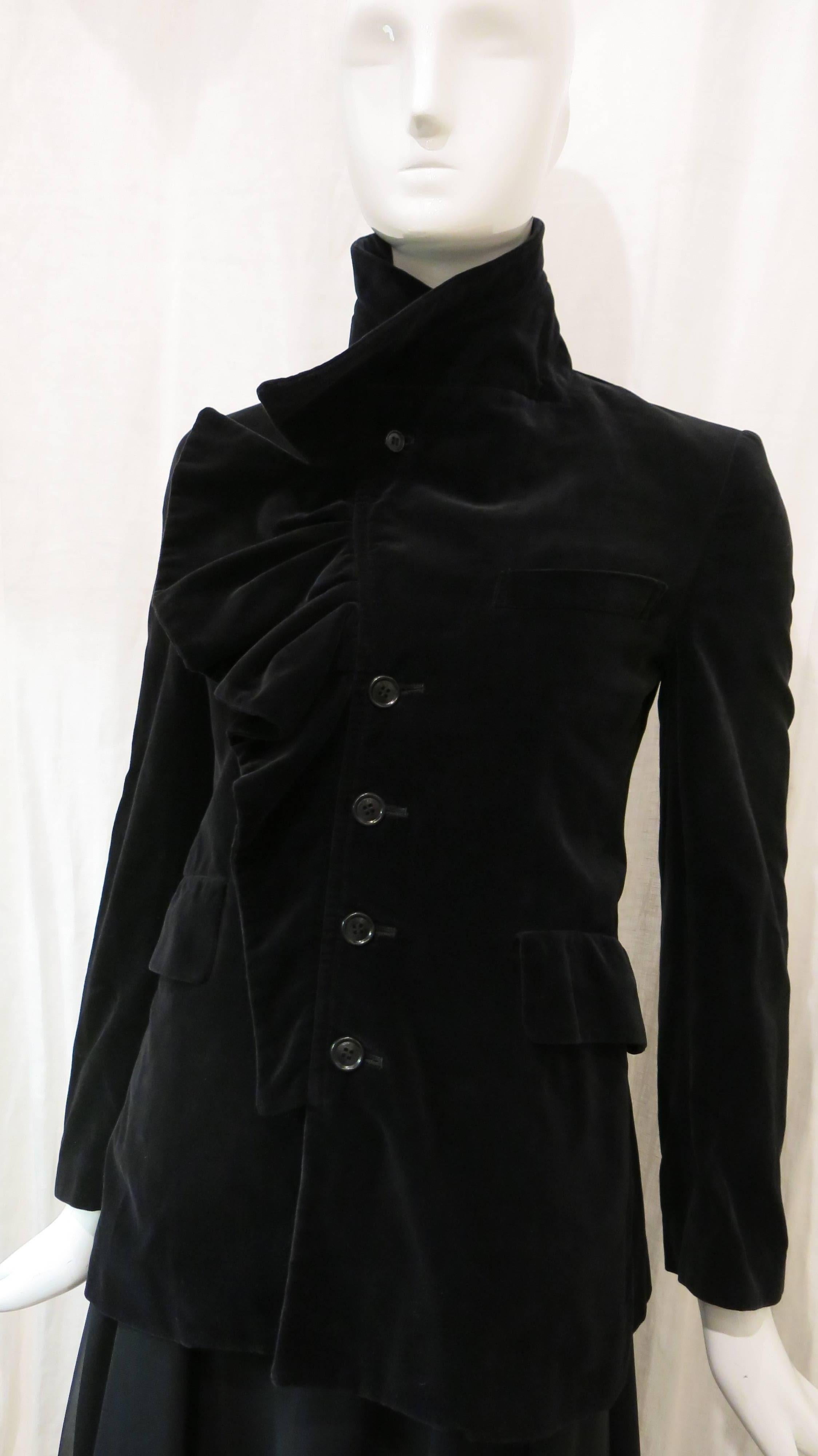 Black velvet blazer with ruffle trim along the buttons. 4 button closure down front of garment. Open pocket on left breast. Two covered front pockets on either side of the bottom of the jacket. Rope trim on inside of ruffle trim. Button closure