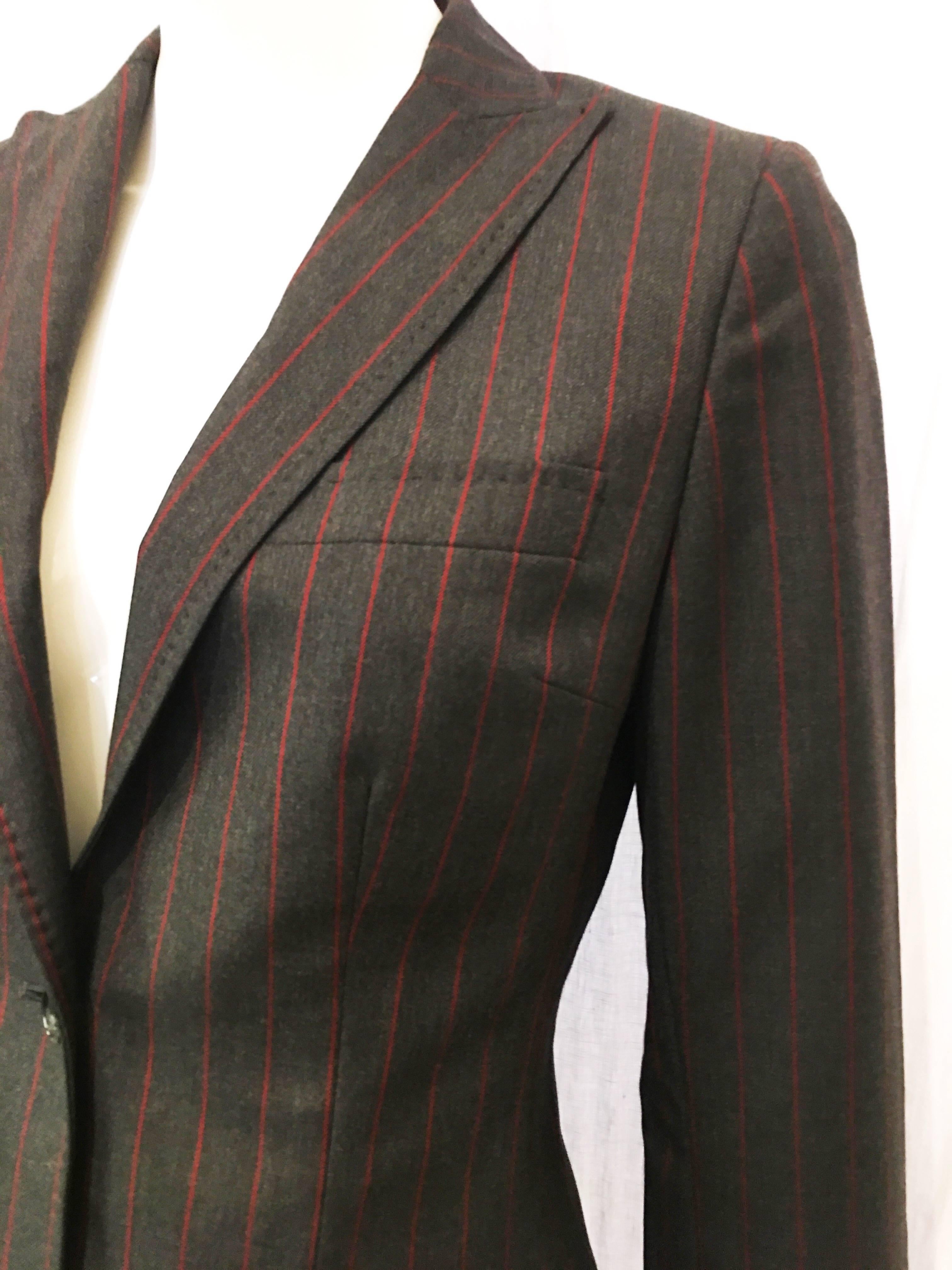 Gray wool blazer with red pinstripes. Sleek and simple design. Four pockets on front of garment- one on left breast, one on left hip, and two at right hip. Jacket is lined with red silk emblazoned with allover Dolce & Gabbana logo. Plaque on chain