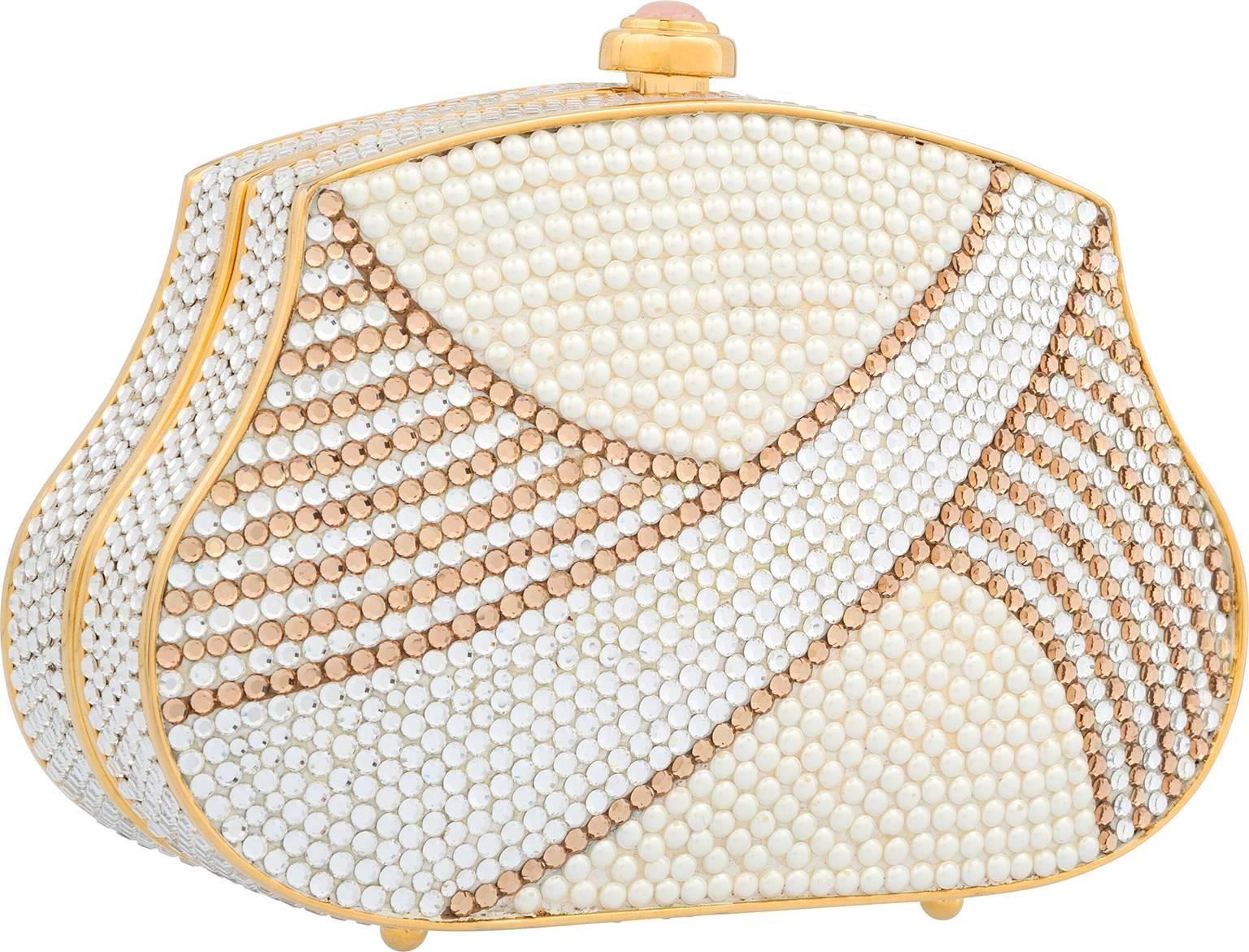 The perfect neutral eveningwear accent, this minaudiere is a great addition to a subtle glamorous look. Done in silver and gold crystals, featuring glass pearl accents, this minaudiere is a great way to add a quiet and quaint luxurious accessory to