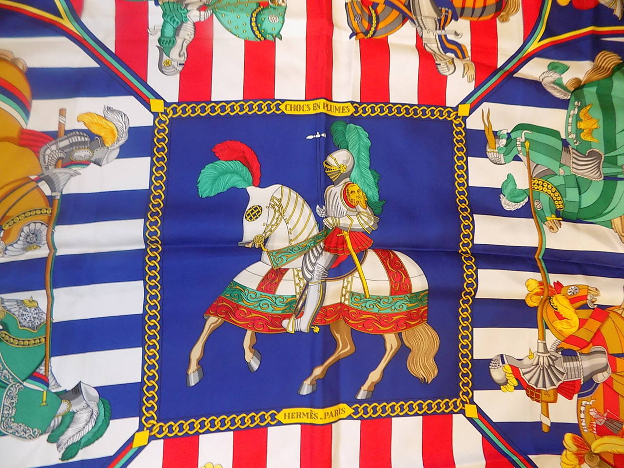 This is a chic and luxurious  Hermes Silk Chocs en Plumes Scarf royal  blue. border. This stylish scarf is 100% silk and features a graphic design of knights on chargers.  This scarf is in excellent, mint condition throughout. 35''by 35