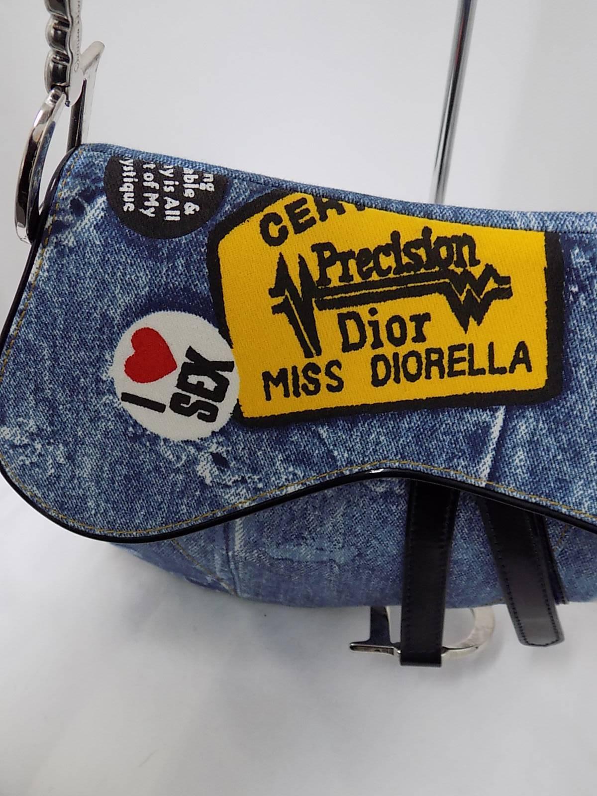 This hot Christian Dior Miss Diorella Denim Saddle Bag is a limited edition piece. This popular style features a sleek saddle design in denim canvas with a jean print and chunky CD hardware on the handles and an over sized dangling 