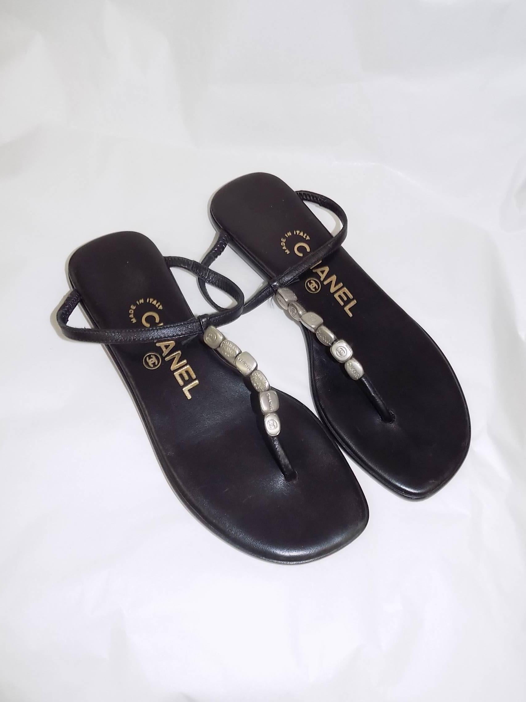 Black leather Chanel thong sandals with silver-tone logo bead embellishments, tonal stitching and stacked heels. Includes dust bag. Condition: Very Good. Faint wear at soles.Size 35