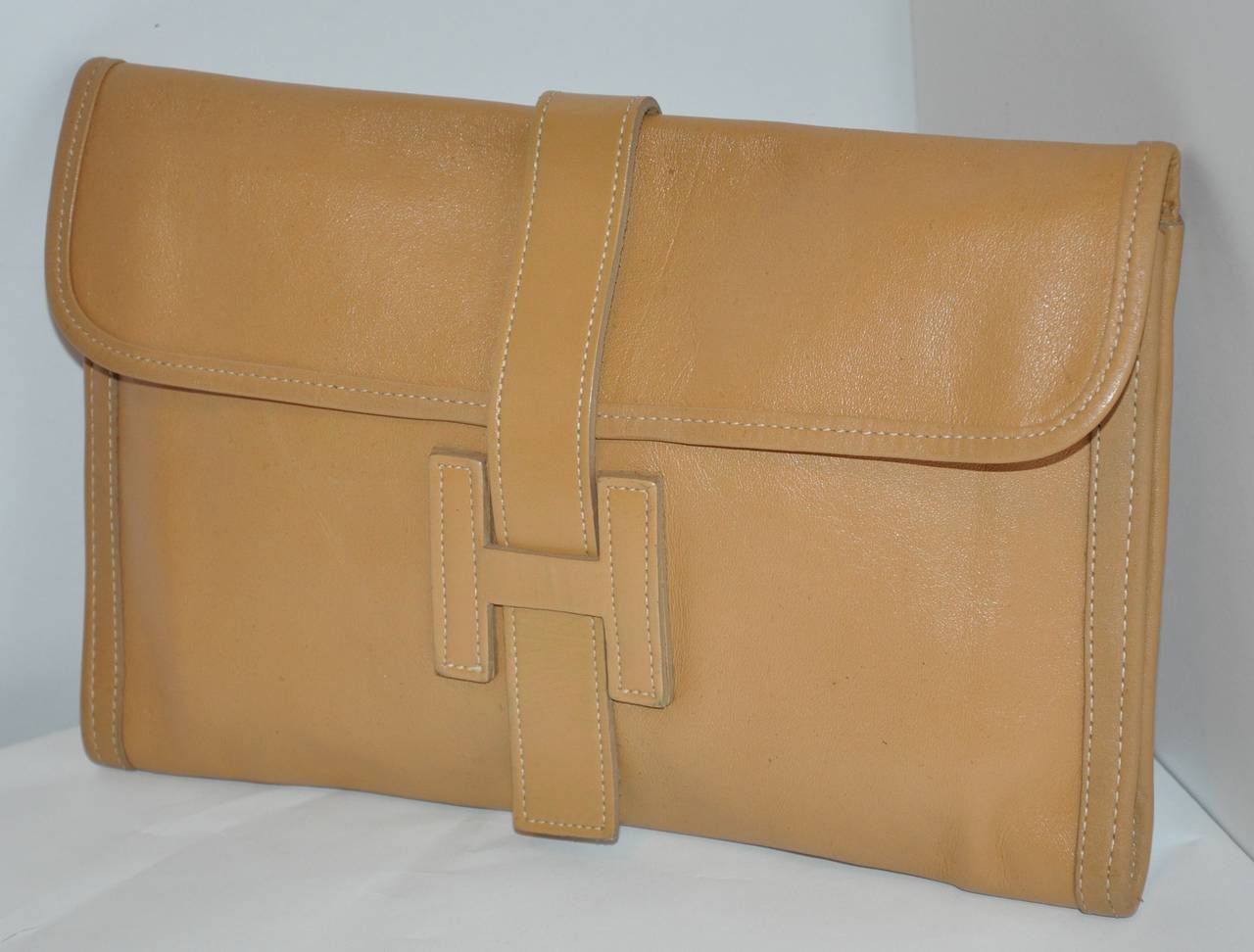 This wonderfully soft lambskin leather tan clutch has detailed top-stitching along with a huge "H" for slipping the closing strap into. 
   The clutch measures 11 1/2" x 7 1/2" in height.