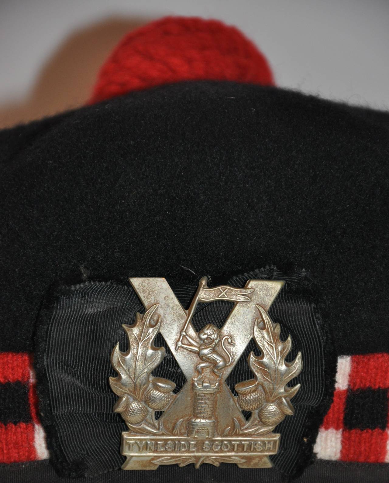        This wonderful detailed wool checkered of colors of black, red and white is accented with a wide silk weave ribbon on back. The center front is highlighted with the crest "Tyneside Scottish" in silver hardware emblem measuring 2