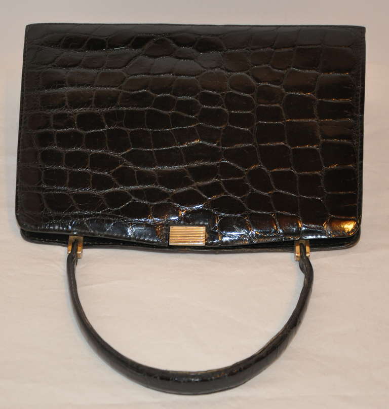 Triopmhe (France) Black calfskin embossed croc leather handbag is highlighted with gold hardware. The bottom of the handbag has gold hardware feet for added protection and better wear.
   The interior has a zippered compartment along with two open