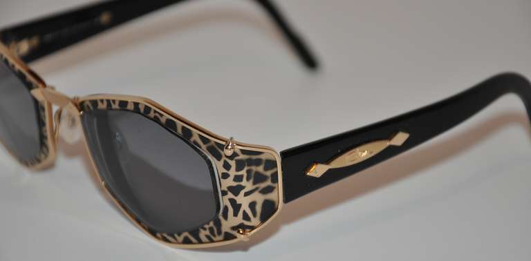 Ces lunettes de soleil merveilleusement méchantes, mais élégantes, sont serties de matériel doré avec un imprimé léopard noir et or sur le devant. Les bras sont en lucite noire et la plaque de signature est en or. Les lunettes sont richement finies