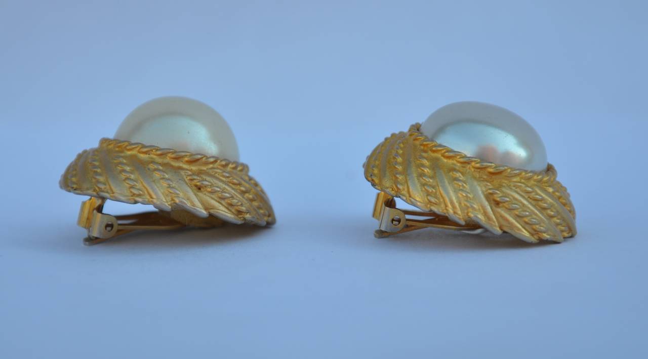 Large gold vermeil clip on earrings is accented with a large pearl center. The gold hardware is etched in details. The earrings measures 1 1/" x 1 3/8" with a depth of 1/2".