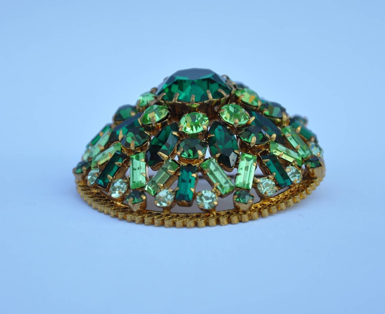 Made in Austria, this wonderfully detailed brooch has gilded gold hardware with filigree touches. The multi-size crystals with multiple shades of greens makes for a wonderful brooch. This brooch measures 2" in circumference with a depth of