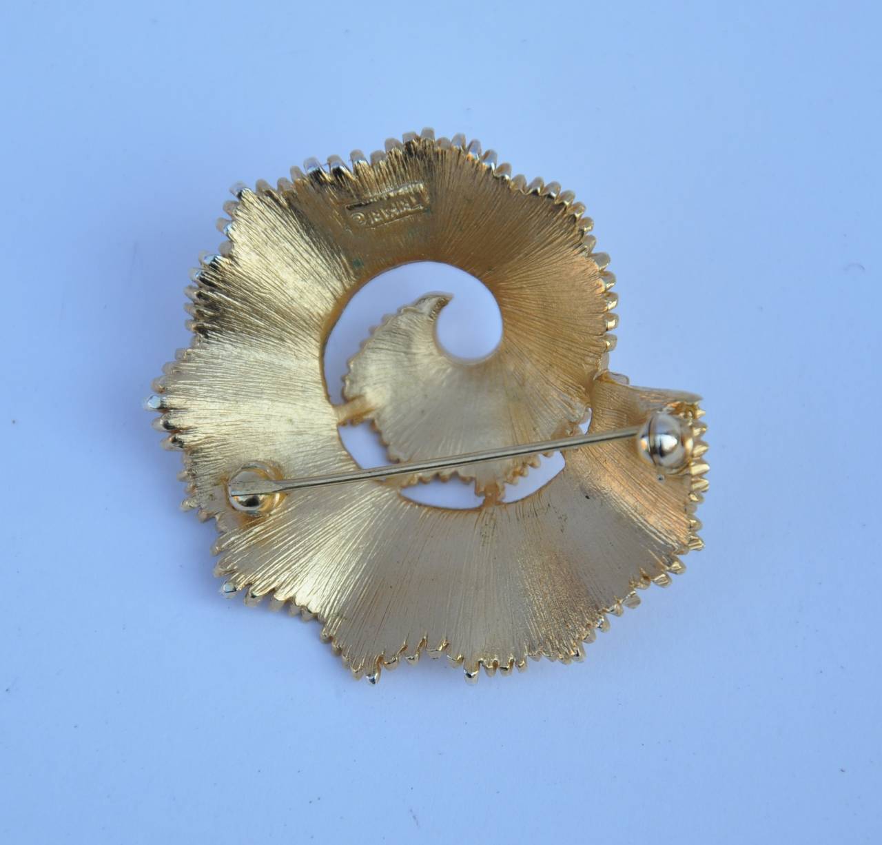 Trifari "Swirl" gold-tone hardware accented with rhinestone brooch measures 1 3/4" in length, 1 5/8" in width and 5/8" in depth. Brooch is signed on the back.