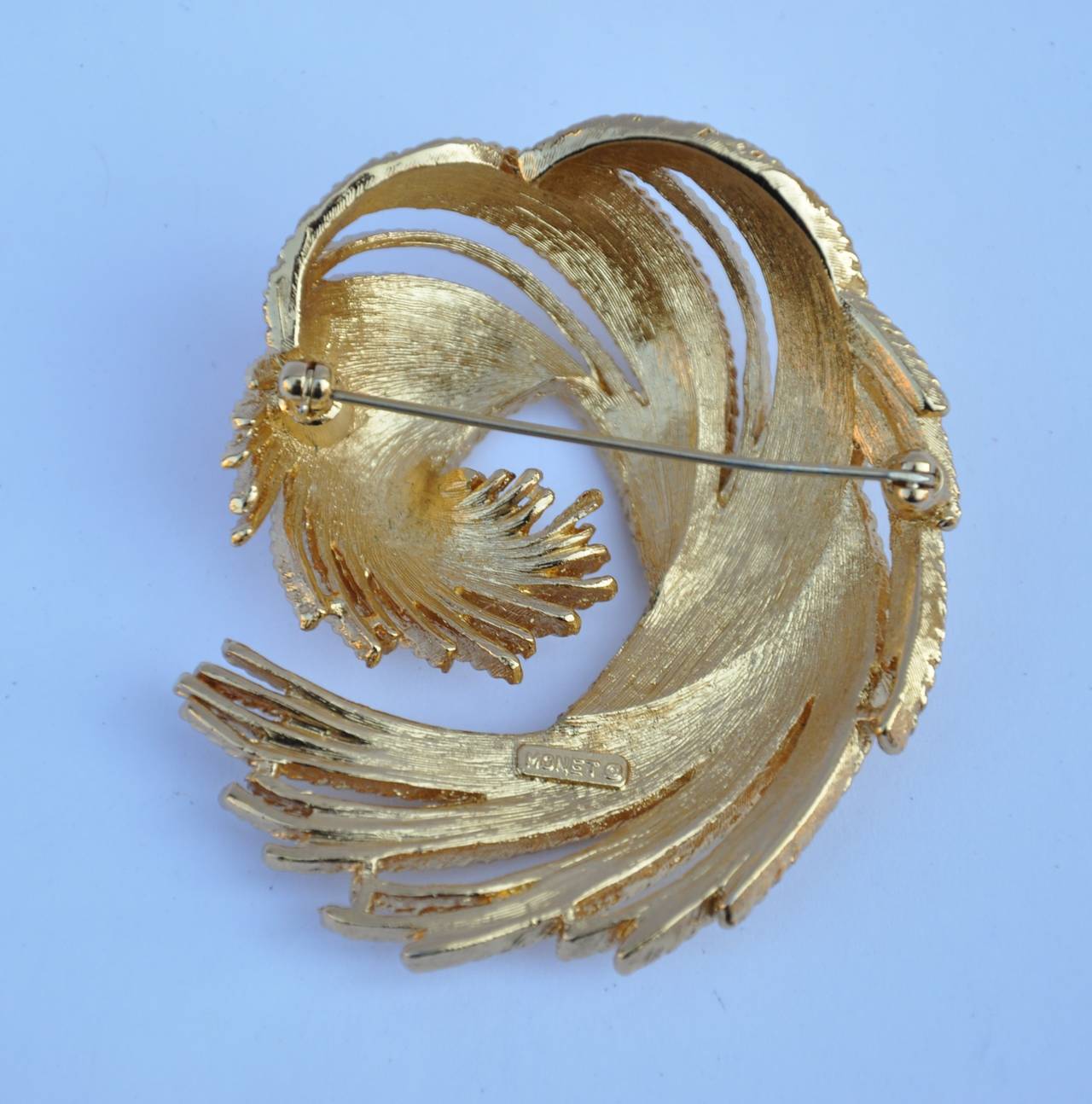 Monet's huge gold hardware "Swirl" brooch is signed "Monet" on the back. The length measures 2 1/2", width is 2", depth is 3/4".