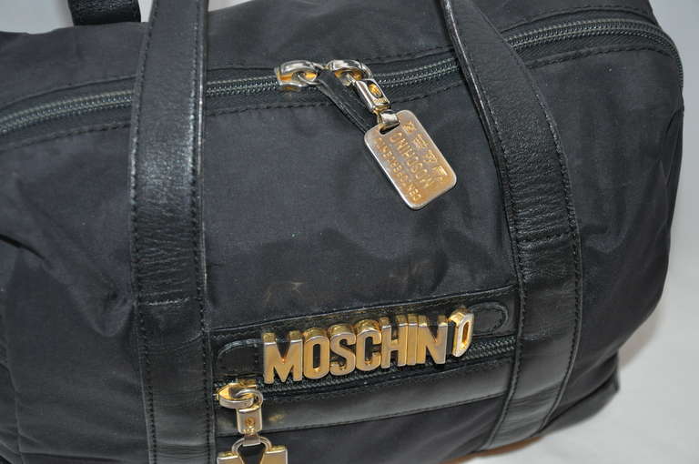 Moschino's wonderfull black nylon tote handbag has a zippered top and accented with their signature name plate and gold hardware movable name on front. Zipper is accented with the 