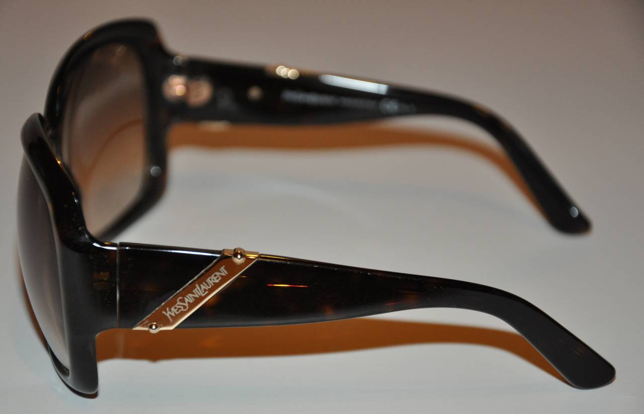 Yves Saint Laurent large black lucite sunglasses are accented with his signature name engraved on gold hardware located on the arms. Gold hardware are throughout with the sunglasses measuring 2 1/4