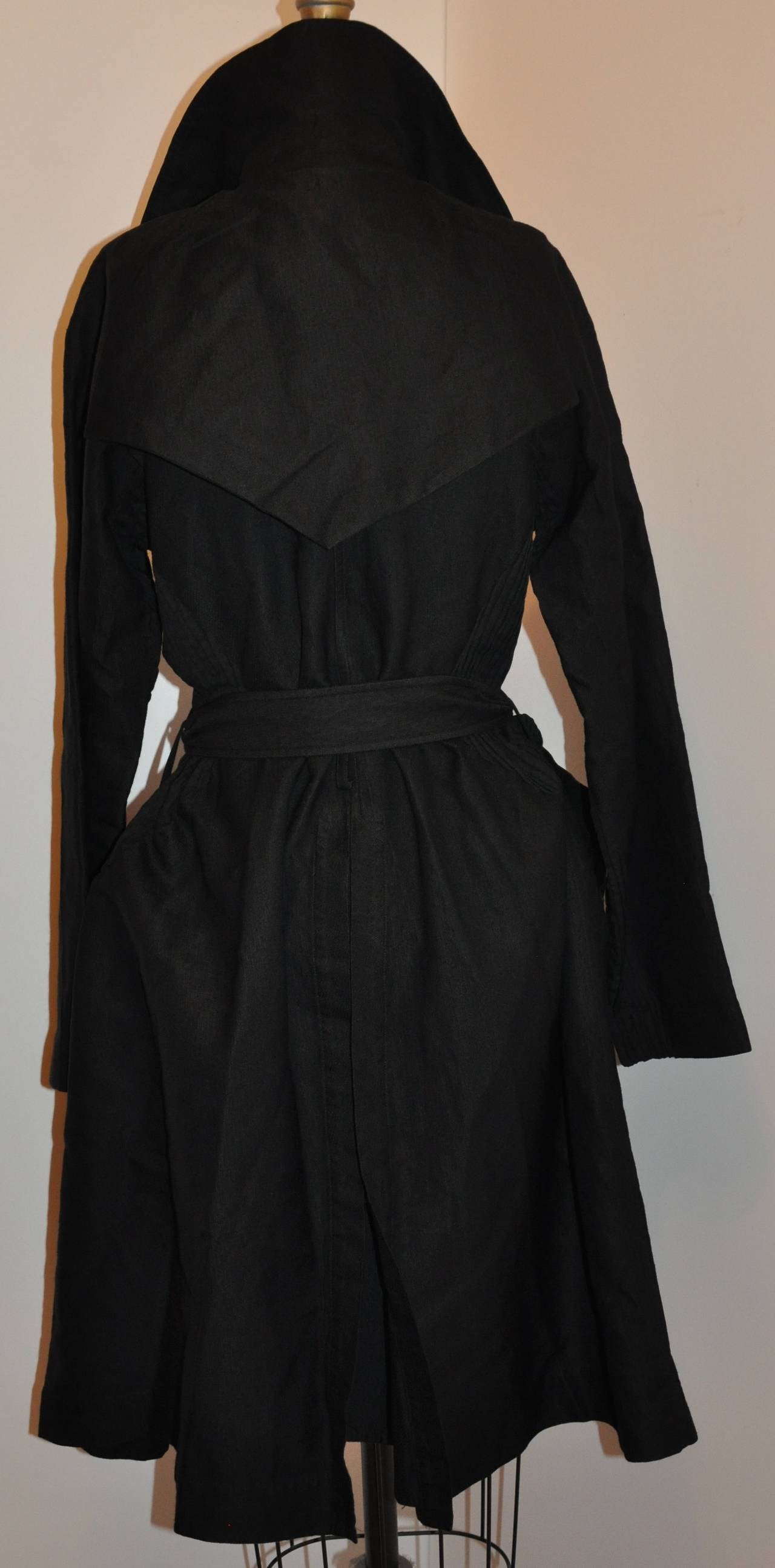 Issey Miyake's wonderfully detailed dramatic black trench-style coat with matching belt is bell-shaped from the waist down with two deep set-in pockets in front. The double-breasted  front has four (4) buttons including the collar which stands at 3