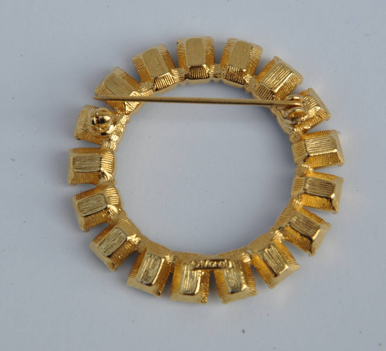 Monet's circular gilded gold with "emerald" rhinestone brooch measures 1 1/2" in height and 1 1/2" in width. Depth is 3/8". Brooch is signed on the backside.