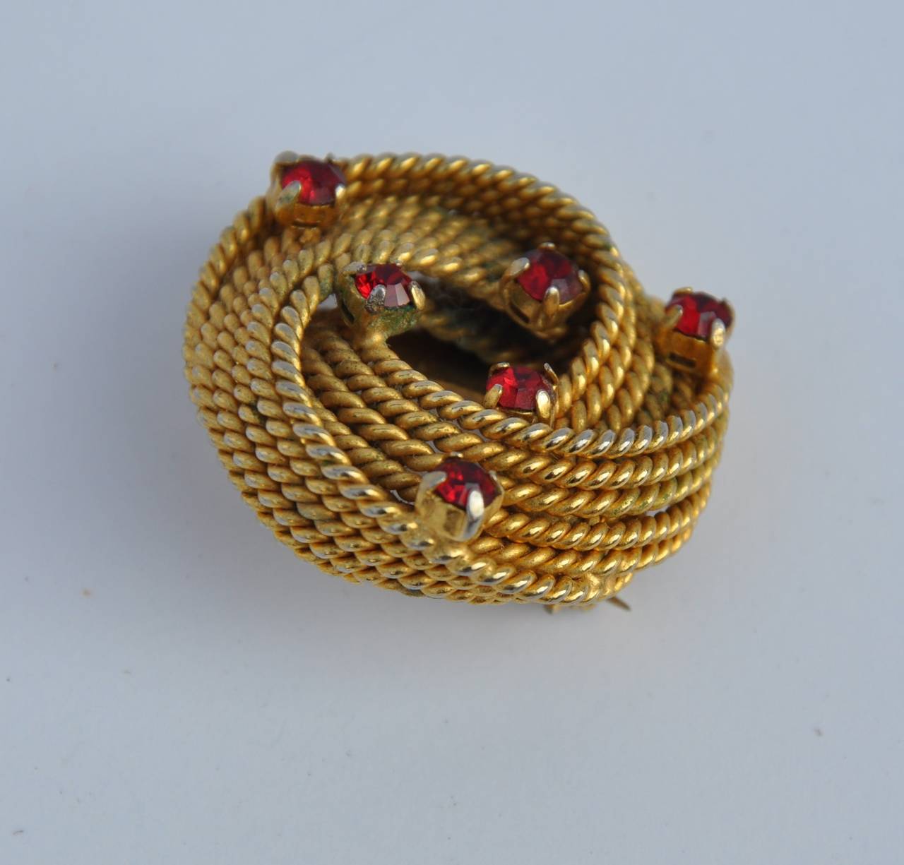 "Twisted Rope" gilded gold hardware brooch is accented with specks of "rubies" rhinestone and measures 1 5/12" in height, 1 1/4" in width and 1/2" in depth.