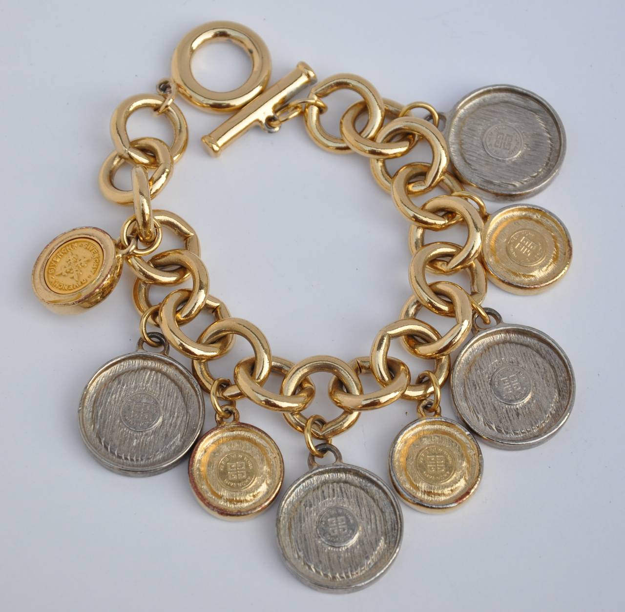 Givenchy gilded gold hardware multi-size coin charm bracelet measures 8" in length, width is 1 3/4" depth is 1/8". Each of the eight coins are signed on the backside.