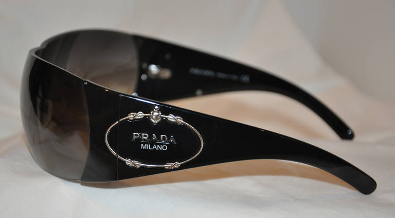 These Prada wraparound black sunglasses are accented with Prada's signature logo on the sides in polished silver.
   The front measures 5 1/2