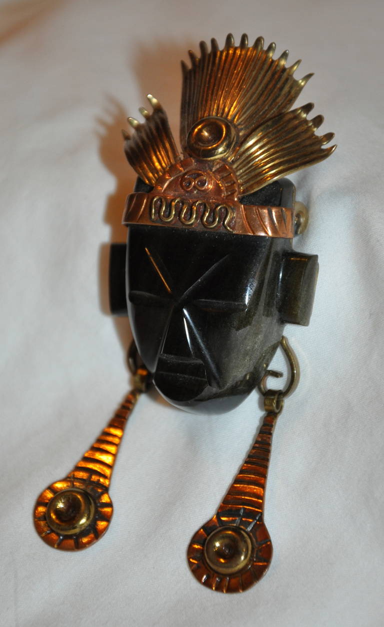 La broche du masque facial en obsidienne et onyx noir est dotée d'une quincaillerie bicolore en finition dorée et cuivrée. La broche mesure 35 mm x 34 mm. La longueur est de 3 1/4