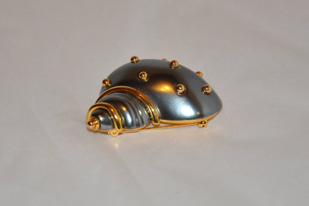 Kenneth Jay Lane, who recently left us, created this wonderfully whimsical and elegant Sea Shell in steel-gray accented with gold studs brooch measures 2 1/2" in length, height is 1 3/4", depth is 1". Wonderfully detail with the