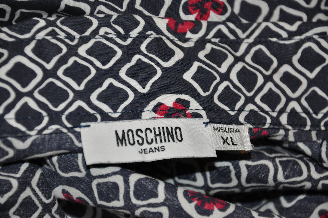 Camicia Moschino da uomo in cotone extra large con colori navy, bianco e rosso. La parte anteriore presenta sette (7) bottoni con il nome della loro firma. Il polsino della manica ha un unico bottone.
   La parte anteriore misura 28