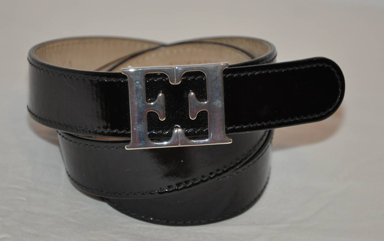 Escada's black patent belt is combined with their signature EE in a silver hardware finish. The belt measures 1