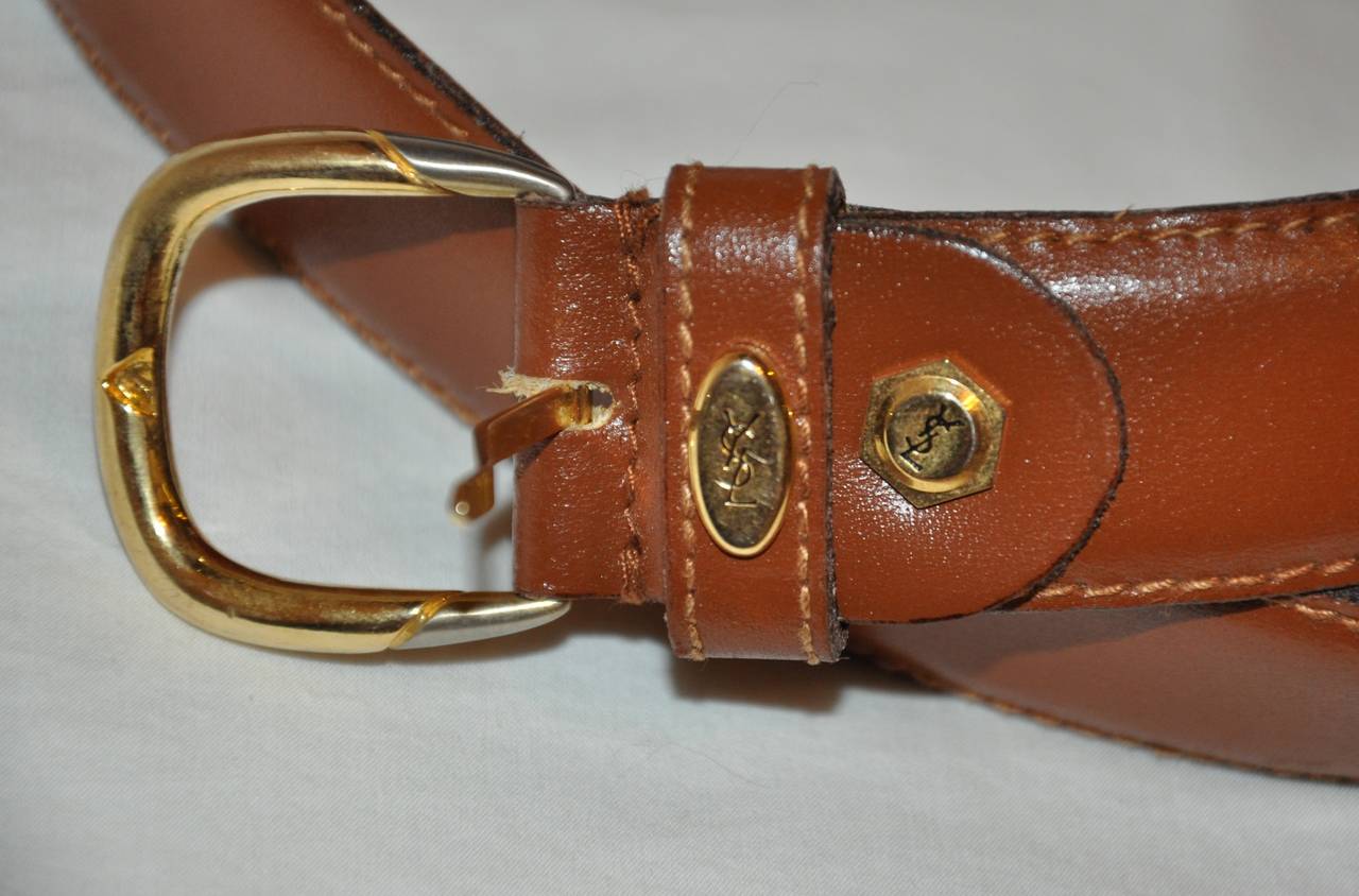 La cintura in pelle di vitello marrone di Yves Saint Laurent è abbinata a una fibbia dorata. La cintura con hardware dorato è incisa con la firma YSL su hardware dorato in due punti, uno sulla cintura e l'altro sull'orecchio della fibbia.
   La
