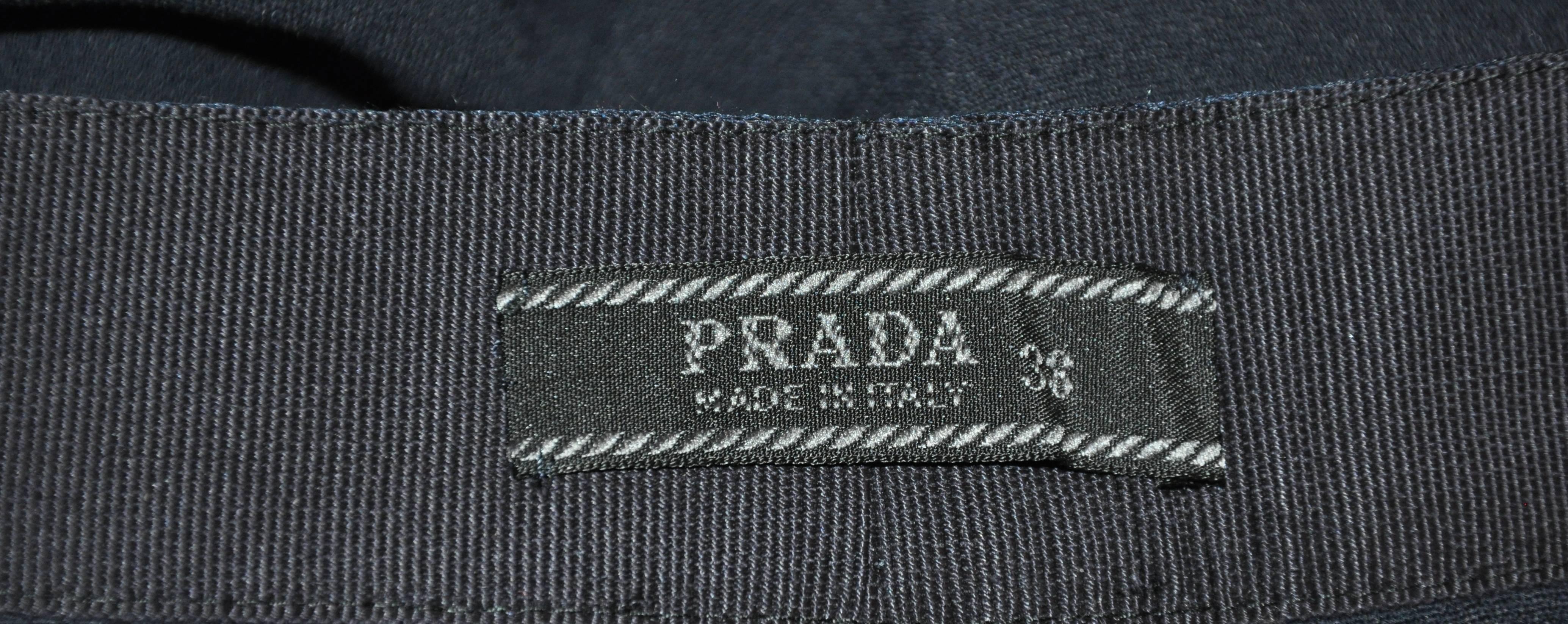           Prada navy tapered trousers are detailed with a silk ribbon waistband which measures 1 1/2