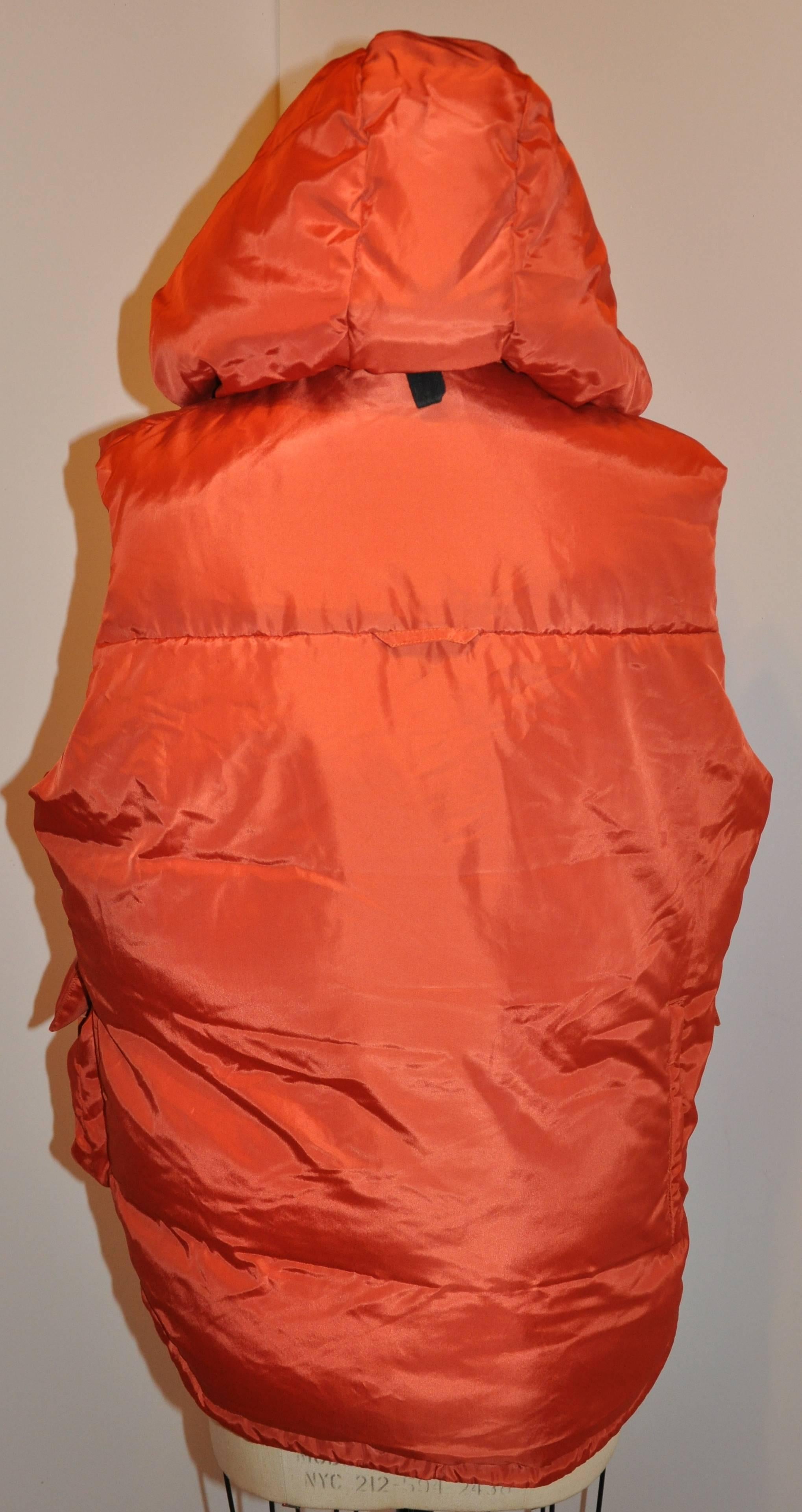          Yoshji Yamamoto wonderfully bold tangerine men's zippered down-filled vest has a removable zippered hood. The hood is accented with two snaps in front to use when needed. The front has two large patch zippered top pockets as well as a
