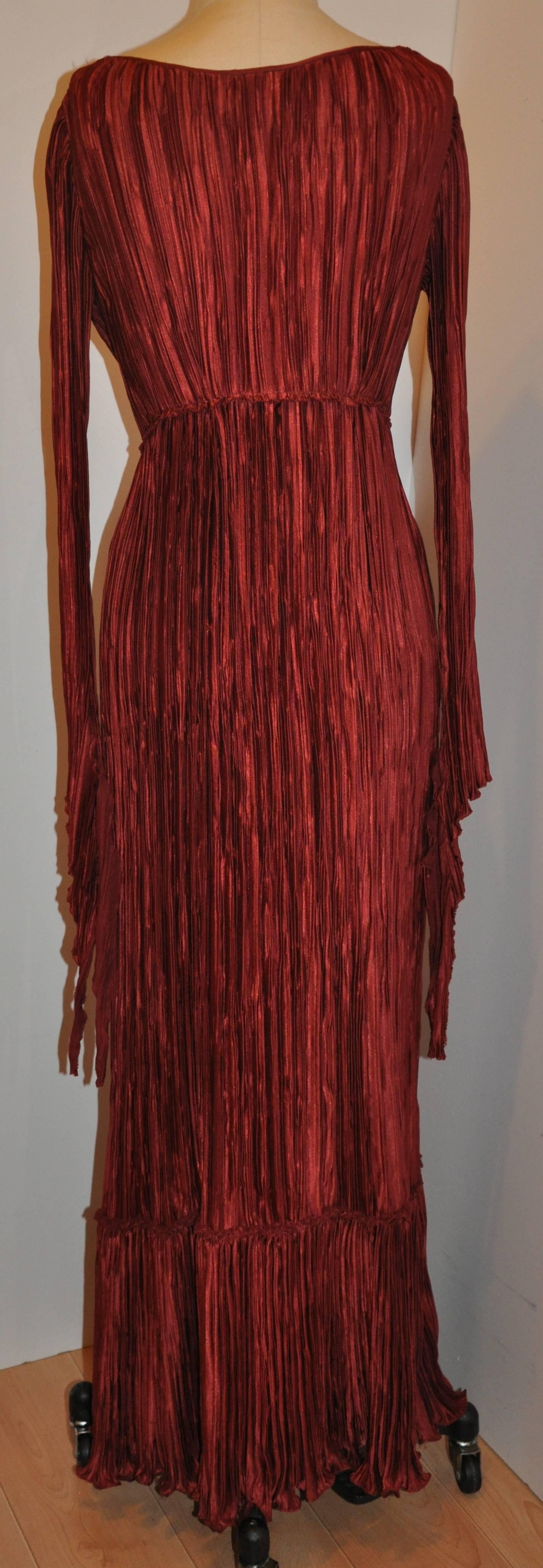         Mary McFadden wonderfully elegant signature pleated body-hugging gown in burgundy is accented with long slim ties on both sleeve's cuffs measuring 12 1/4