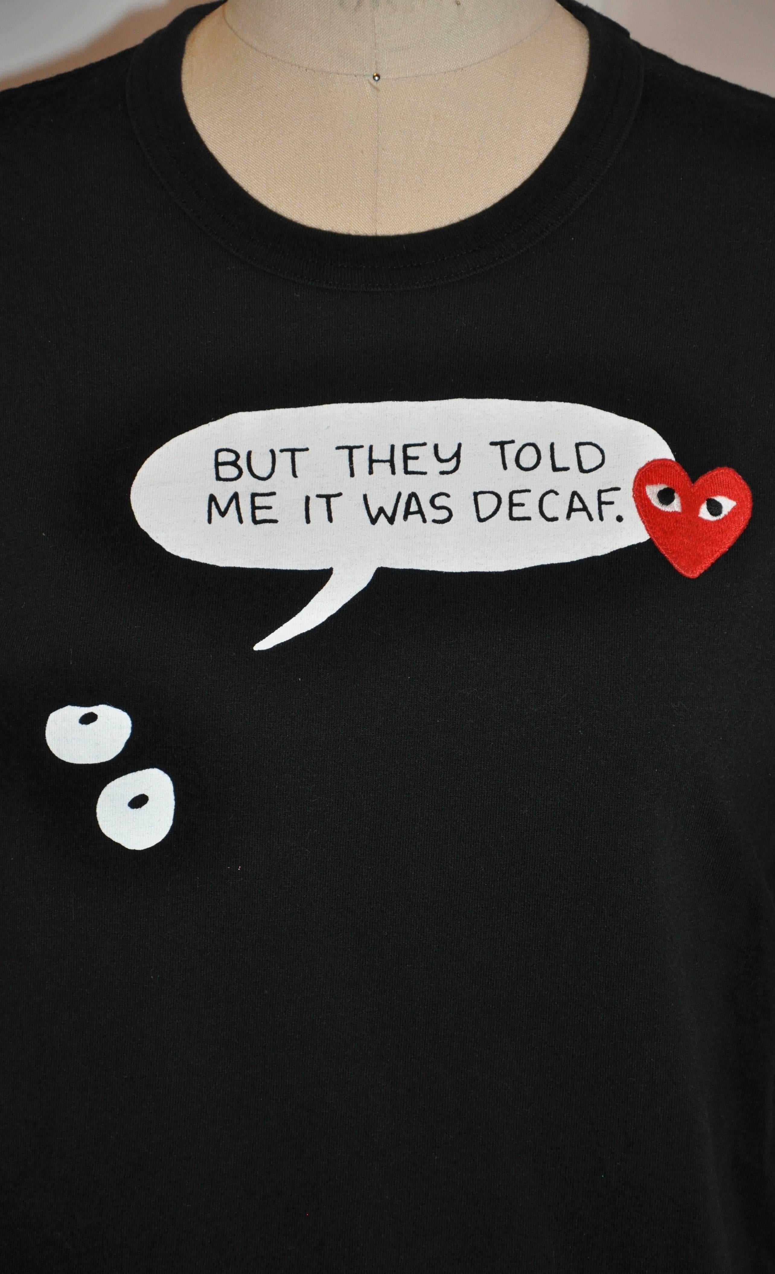            Comme des Garcons whimsical black cotton tee is detailed with print and a embroidered heart with eyes. The front length measures 21 3/4