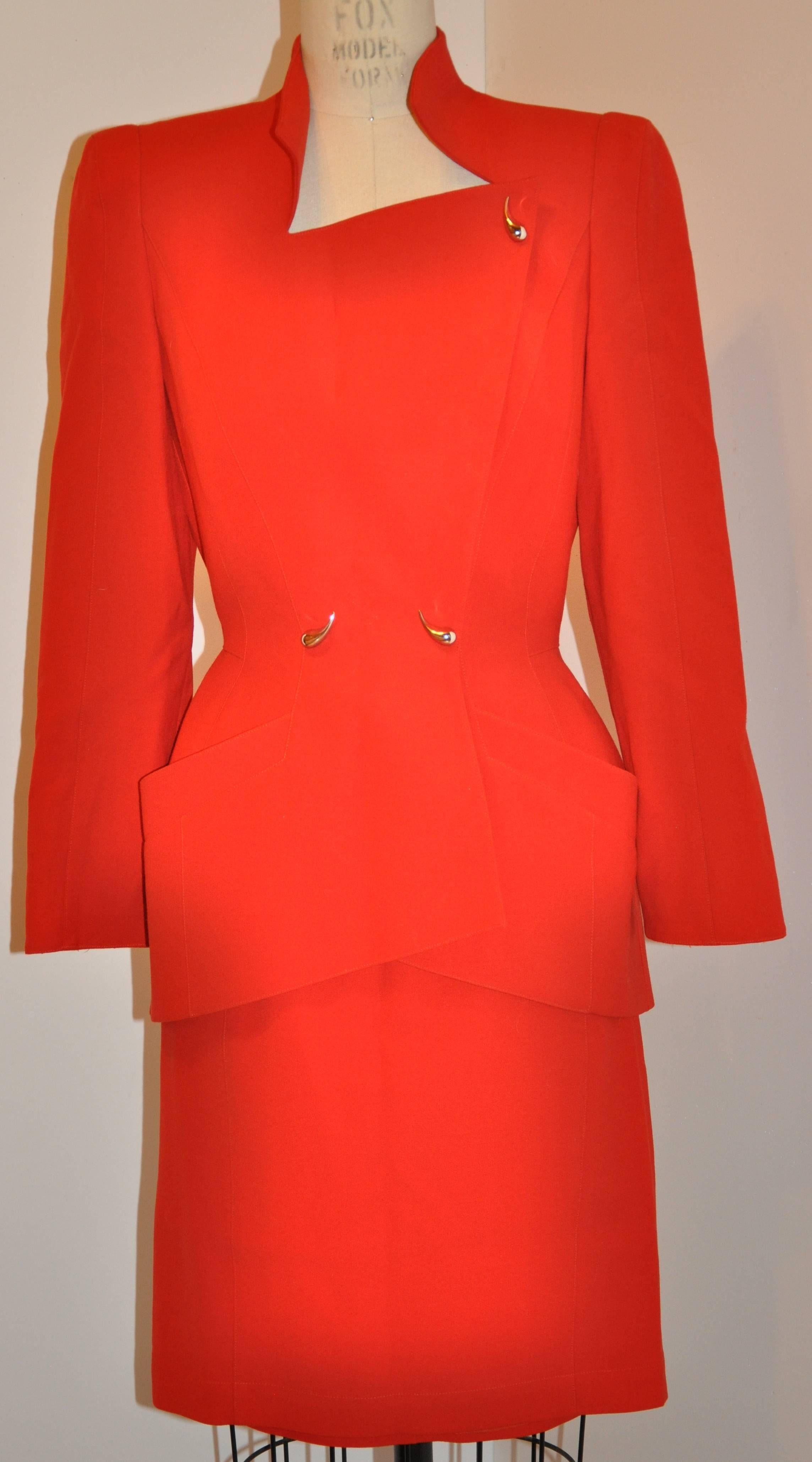        L'ensemble deux pièces à double boutonnage avec boutons-pression, signé Thierry Mugler, est d'un rouge éclatant. Il est orné de surpiqûres et de boutons de citation argentés qui recouvrent les boutons-pression situés sous la jupe. La jupe est