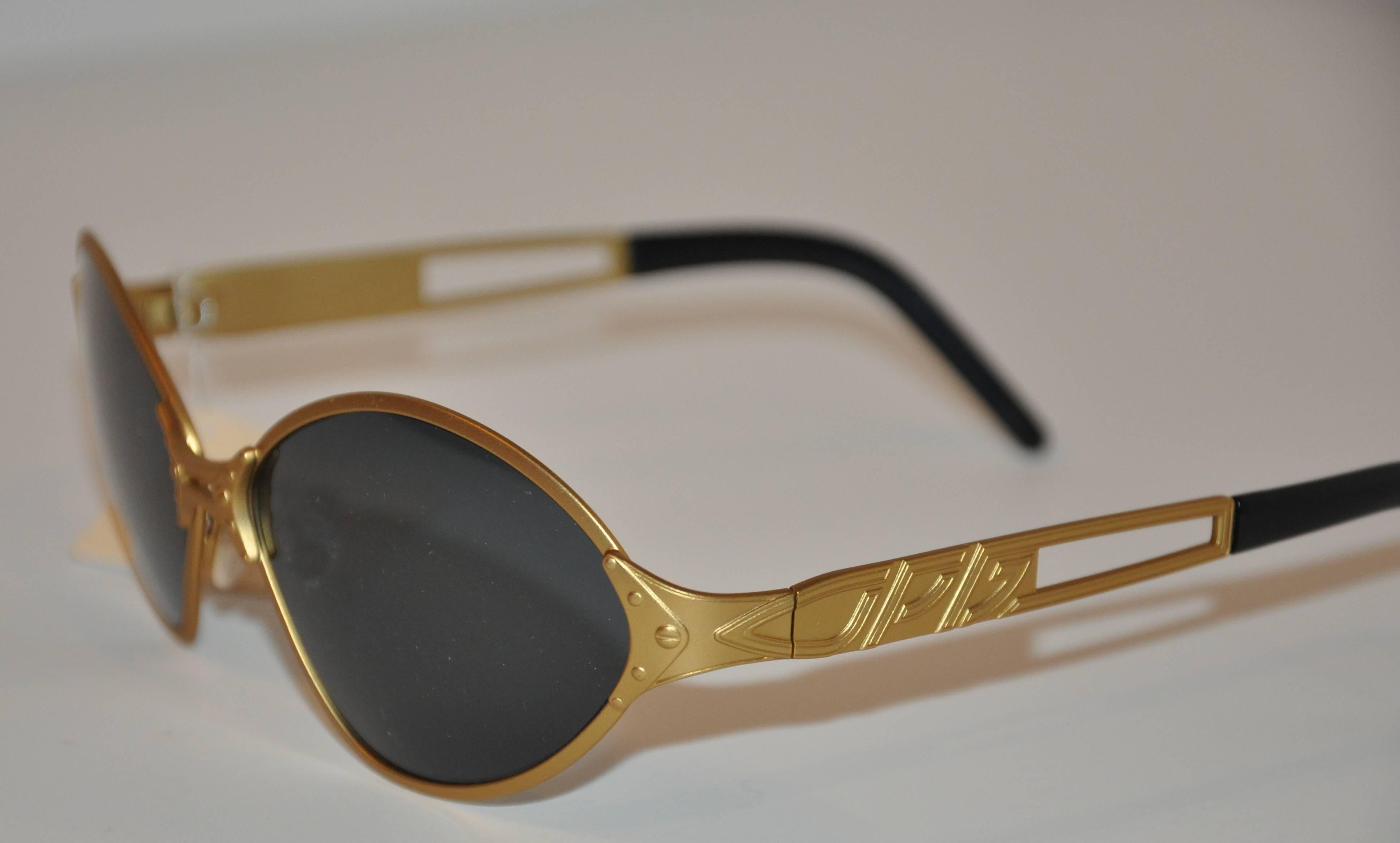 Jean Paul Gaultier wonderfully detailed gold tone sunglasses are detailed with micro-studs on the center-front as well as the corners. The arms are accented with the signature etched nameplate as well. Tips are finished with black lucite. The front