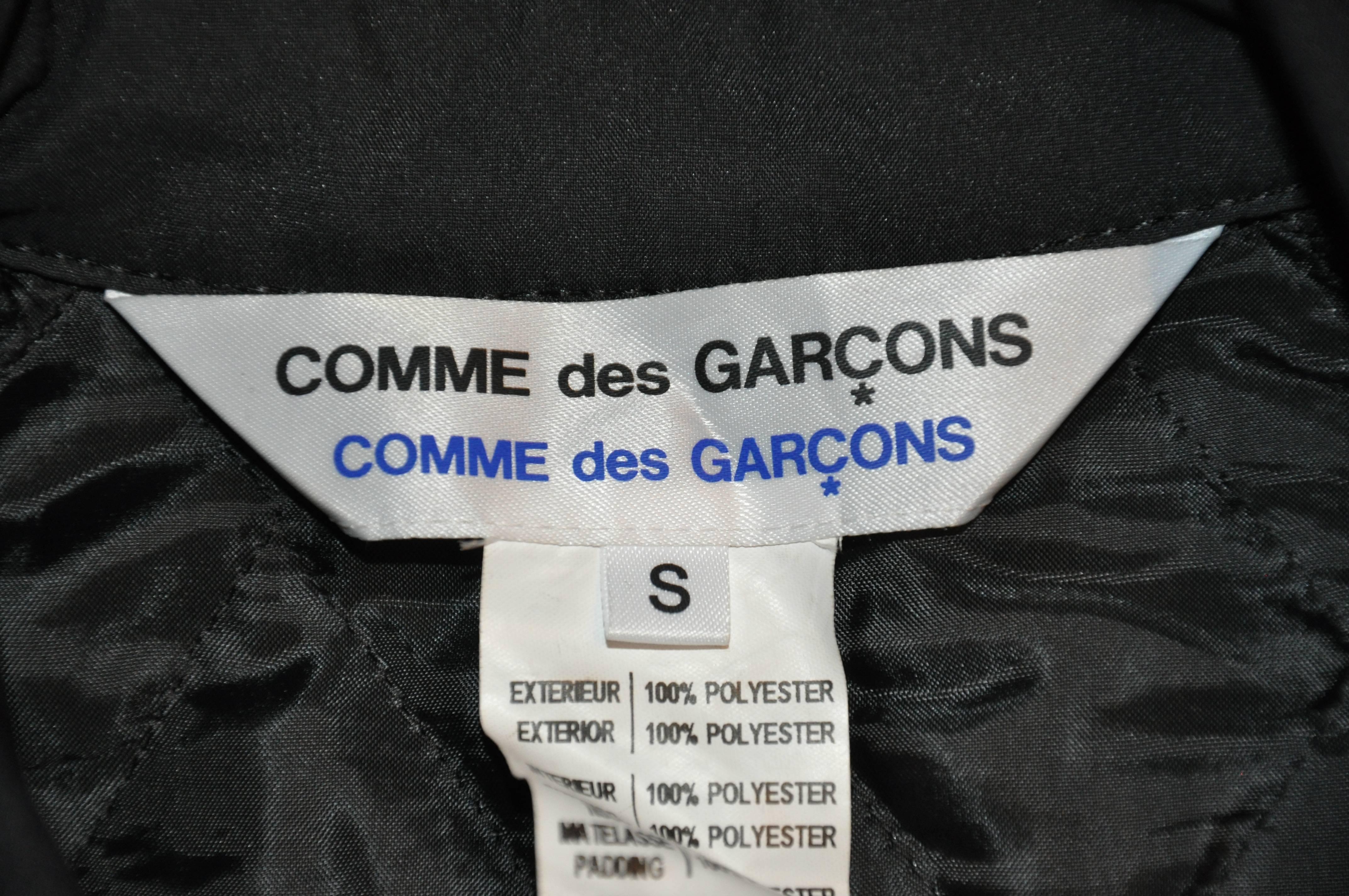        Comme des Garcons 'Comme des Garcons' wicked black nylon with quilted lining zippered motorcycle poncho if accented with two zipper pockets as well as one breast zipper pocket on front. There is also a set-in with a flap and snap closing on