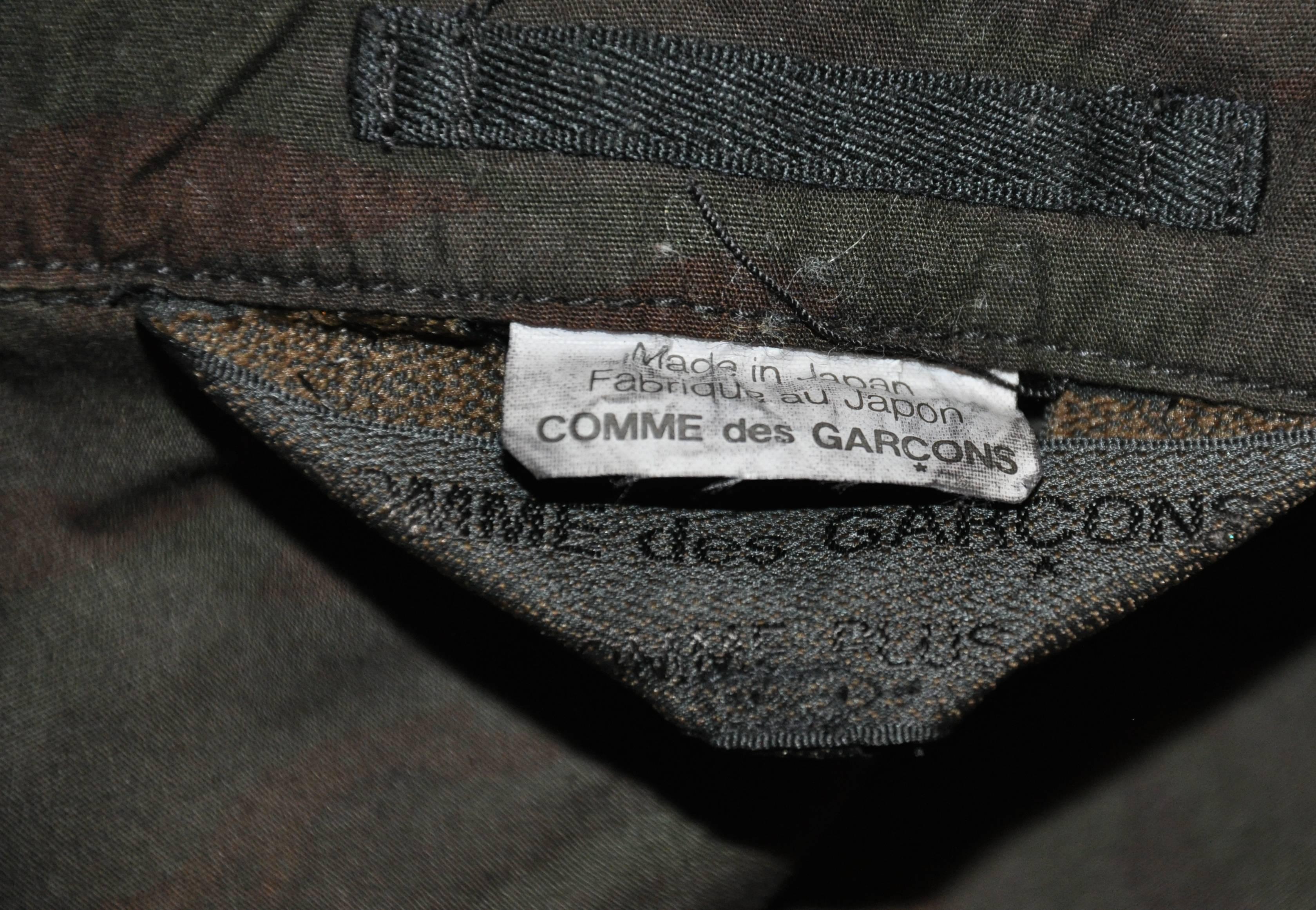        Comme des Garcons camouflage four-button front including a single button for the lapel jacket features multi patch pockets on the front. The waist in enforced on the interior for a better fit. The jacket is detailed with a scallop hem as well