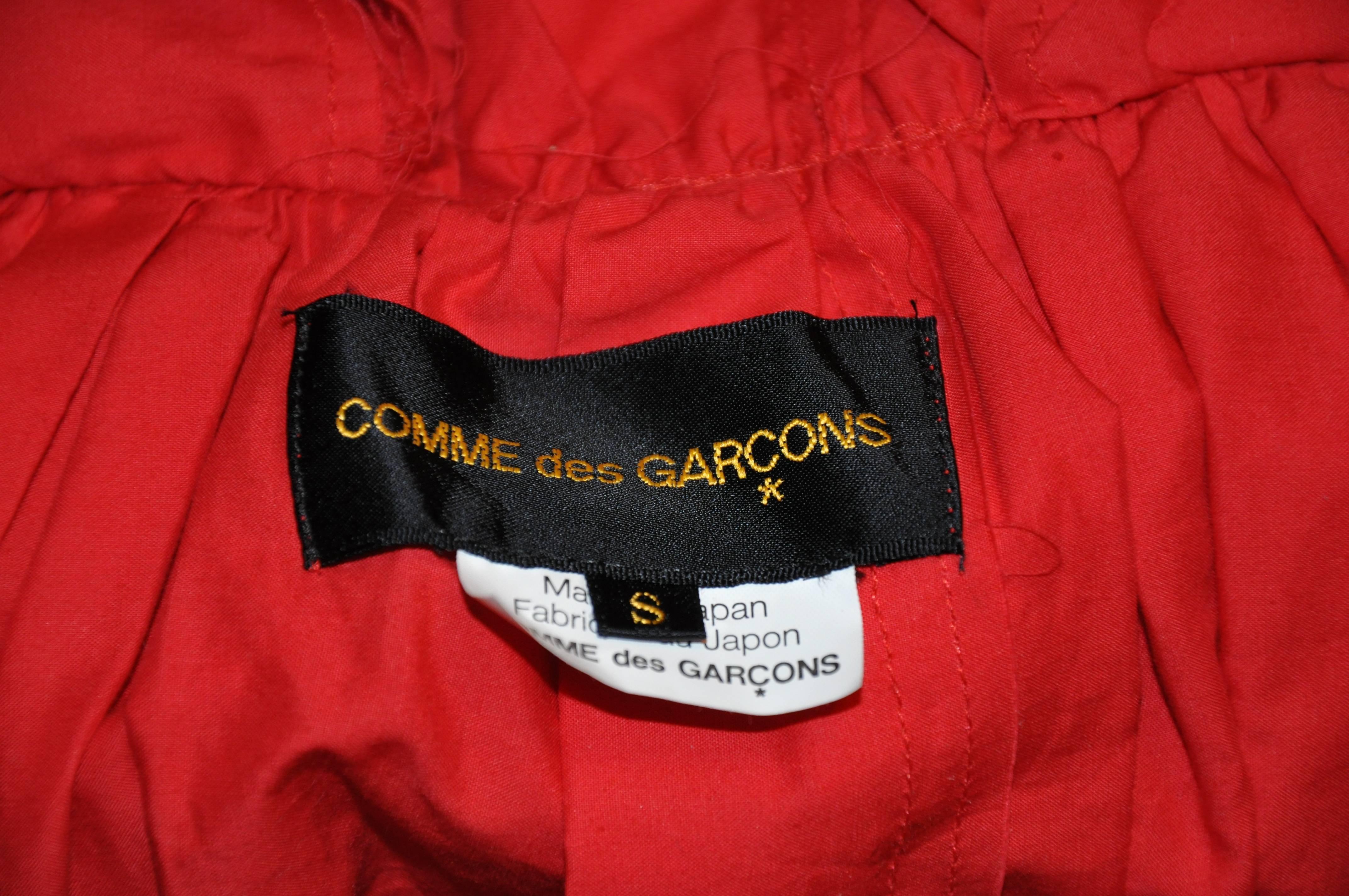        Comme des Garcons wonderfully wicked engine red deconstructed multi-pleated, multi-ruffle crop top detailing two collars. There are two matching buttons in front with detailing deconstructed ruffles along the extended sleeves. Waistband