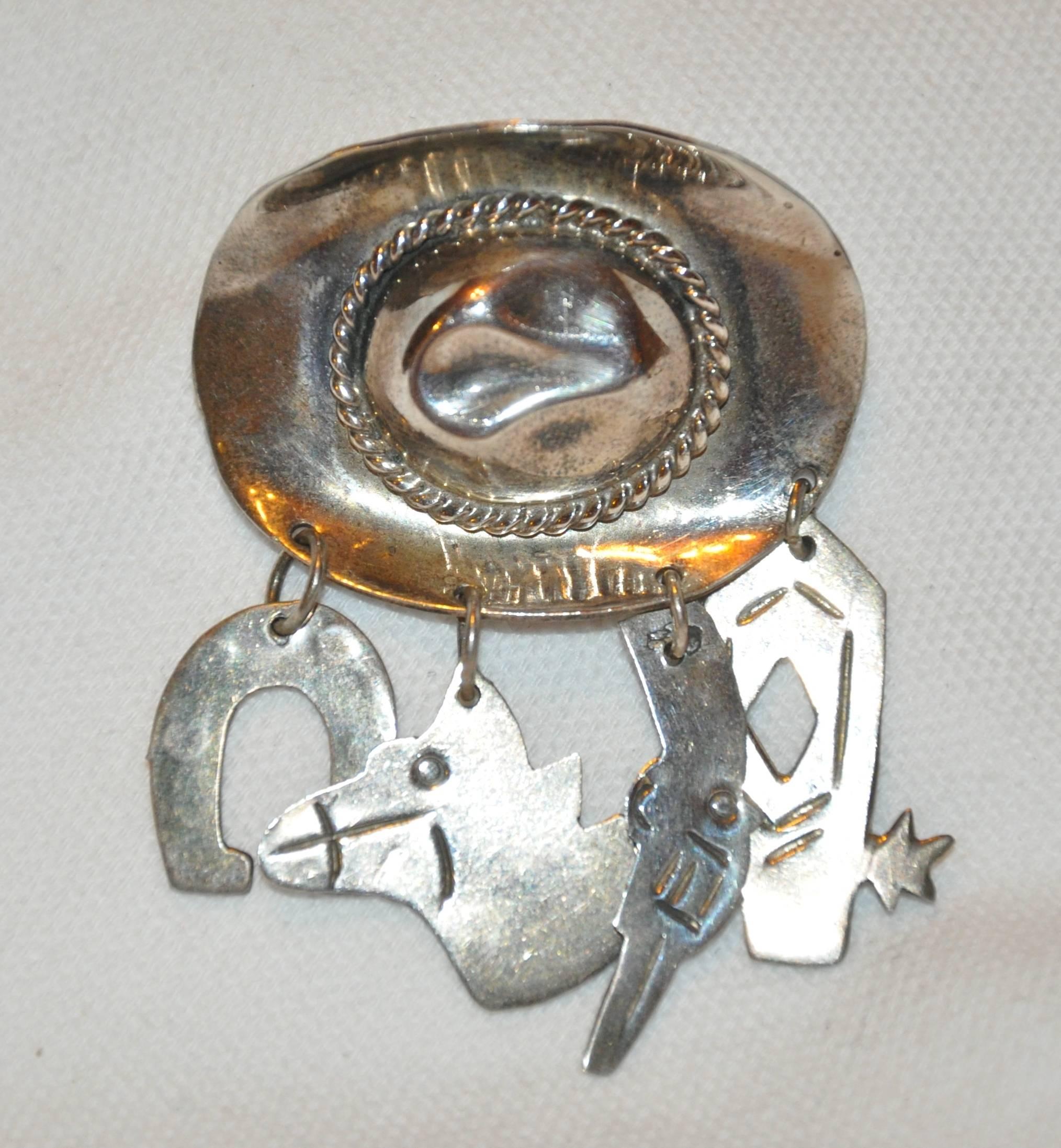       Wonderfully detailed, this "Cowboy Hat" brooch is accented with a cowboy's accessories such as a horse's shoe, gun, boots, and his companion displaying a horse's head dangling below the hat. The hat itself measures 1 7/16" x 1