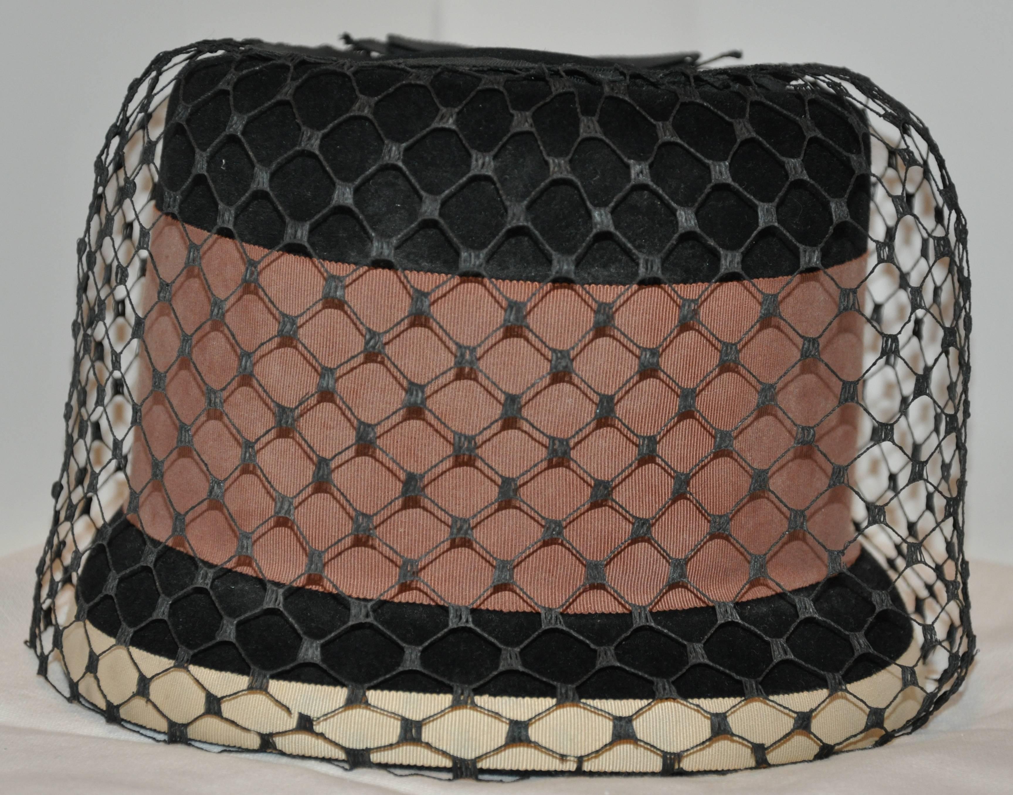           Whimsical Tall black wool felt hat is detailed with a width warm-brown silk cord band as well as a beige silk cord and finished with a wonderful full netted and a simple silk bow on top. The interior circumference measures 21 inches.
