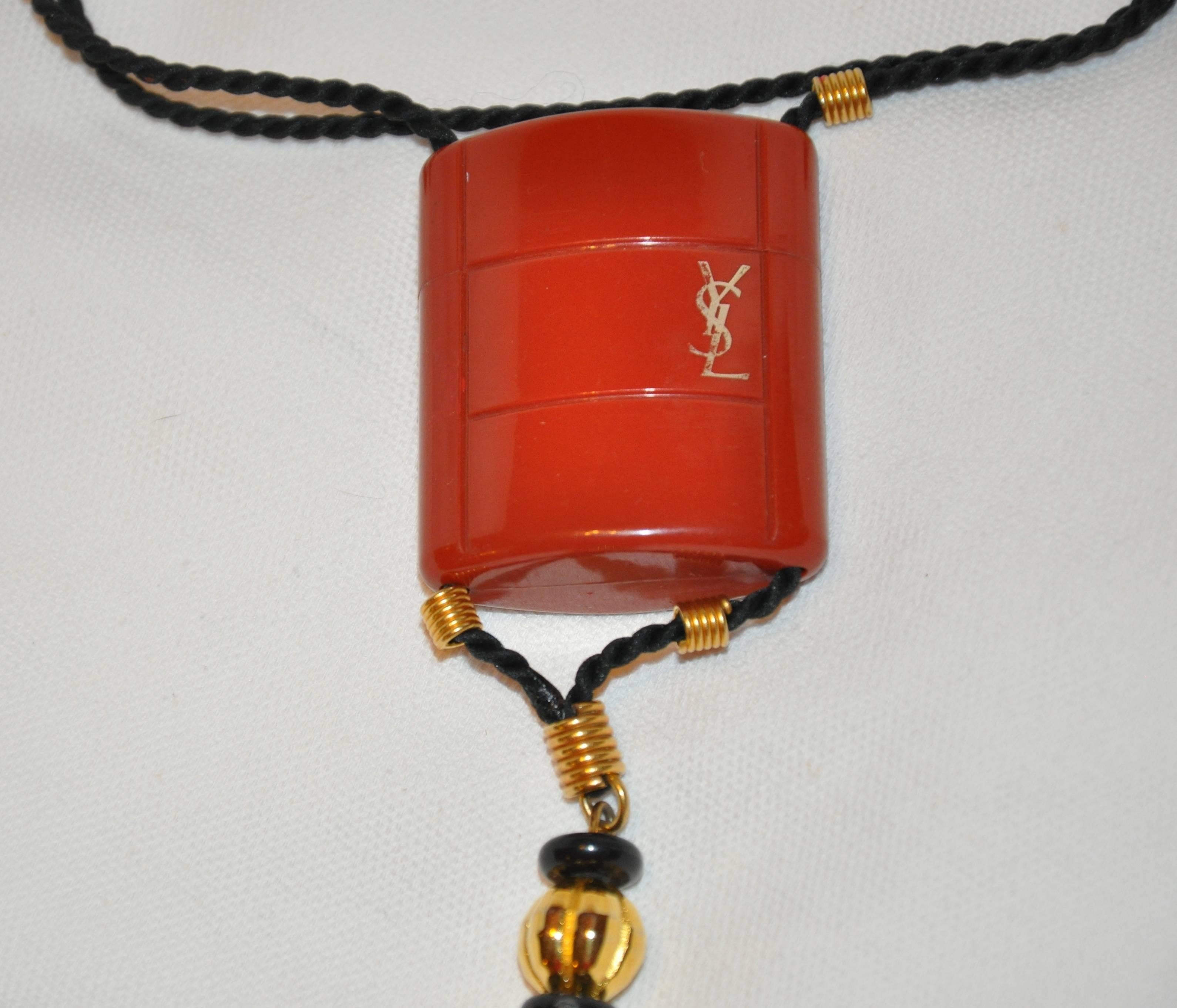        Yves Saint Laurent signature "Opium" collection perfume holder pendant with adjustable black silk cord necklace and black silk tassel detailed with gilded gold accents. The pendant with tassel measures 6 1/2 inches in length and 1