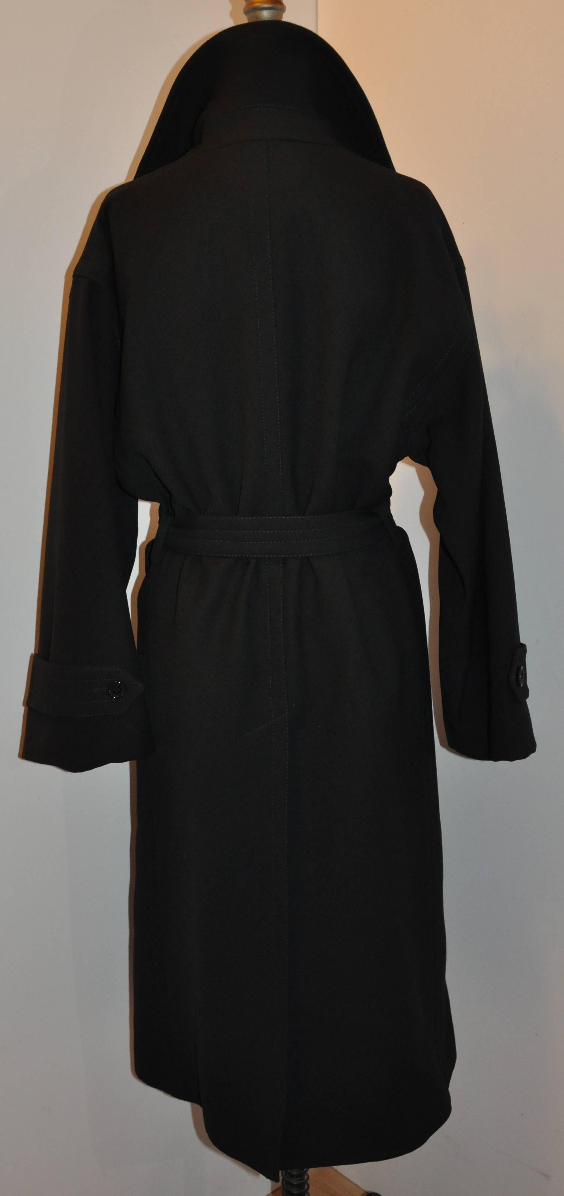        Dolce & Gabbana wonderfully elegant signature black wool gabardine trench coat with matching self-tie belt measures 45 inches in length. The front has two set-in pockets and the center back a long flat vent. Detailed top stitching throughout