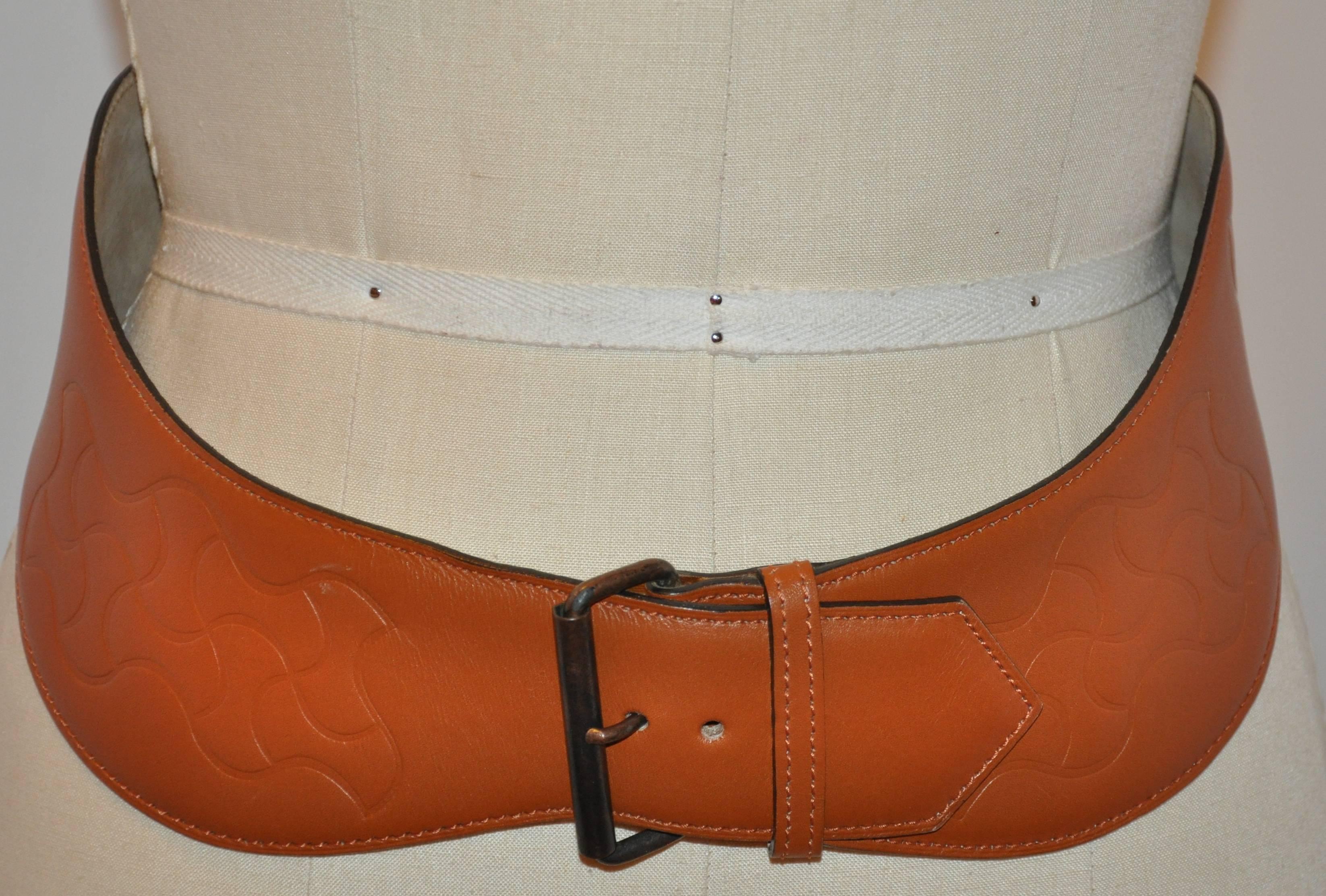        This wonderfully detailed Alaia warm brown curved belt is detailed with embossed accents and measures 2 5/8 inches in width, and finished with top-stitching along the edges. The total length measures 32 inches. Size is 75, made in France.